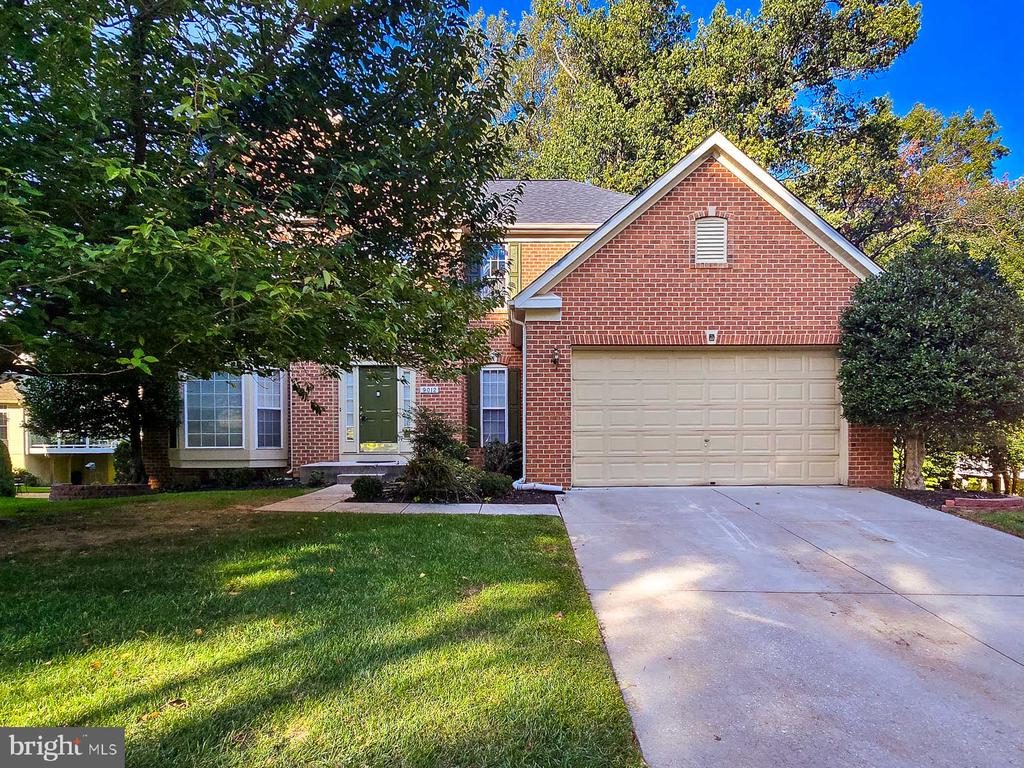 Red brick two-story house with an attached two-car garage, wide driveway, and mature trees.