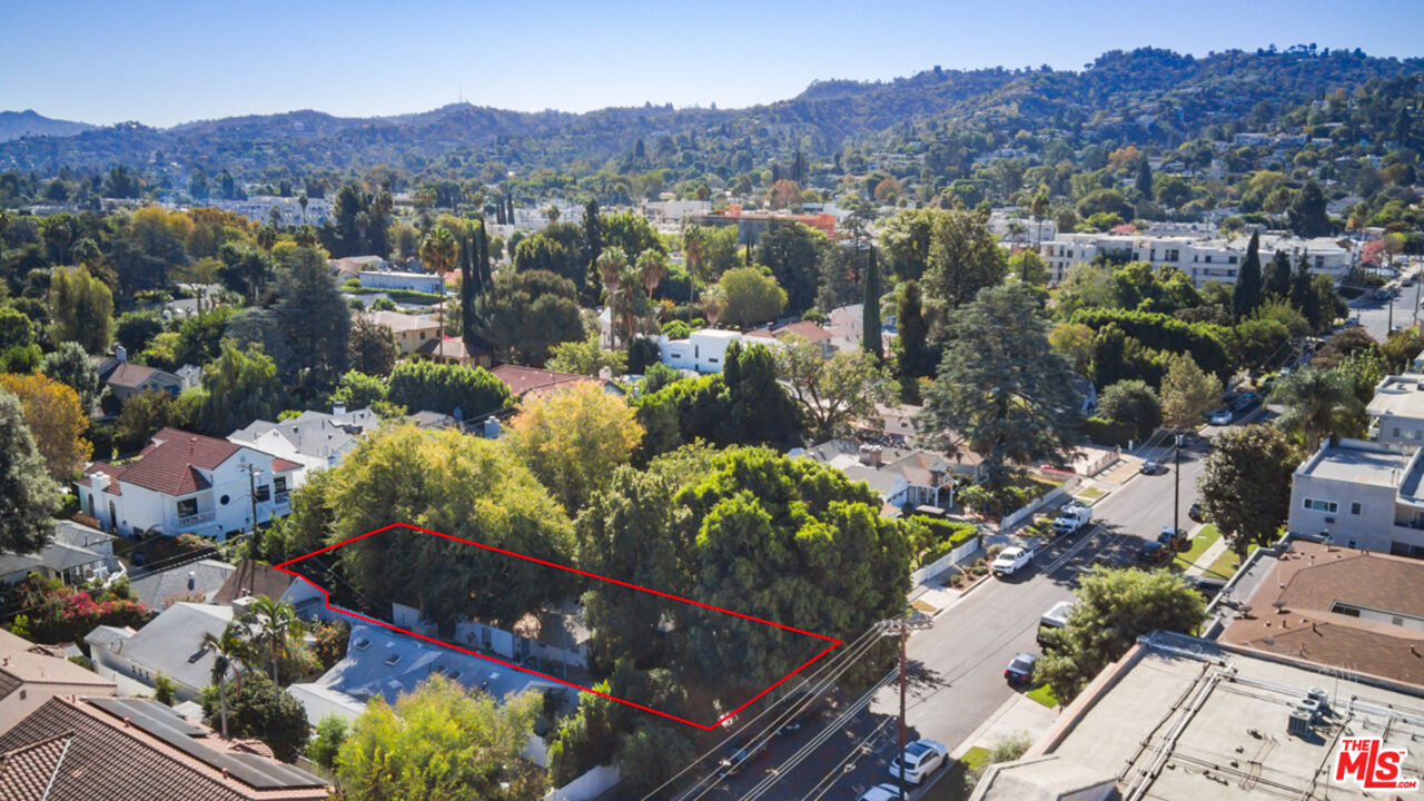 Aerial view of a tree-covered property outlined in red beside a residential street.