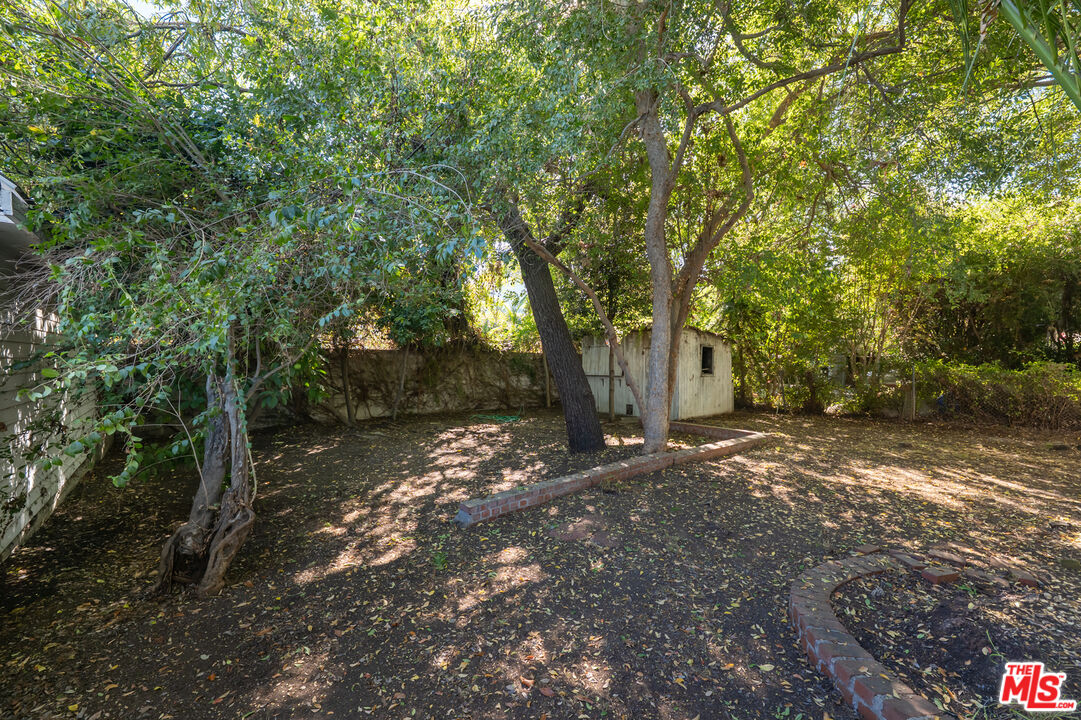 Shaded backyard with mature trees, a small shed, and curved brick garden edging.