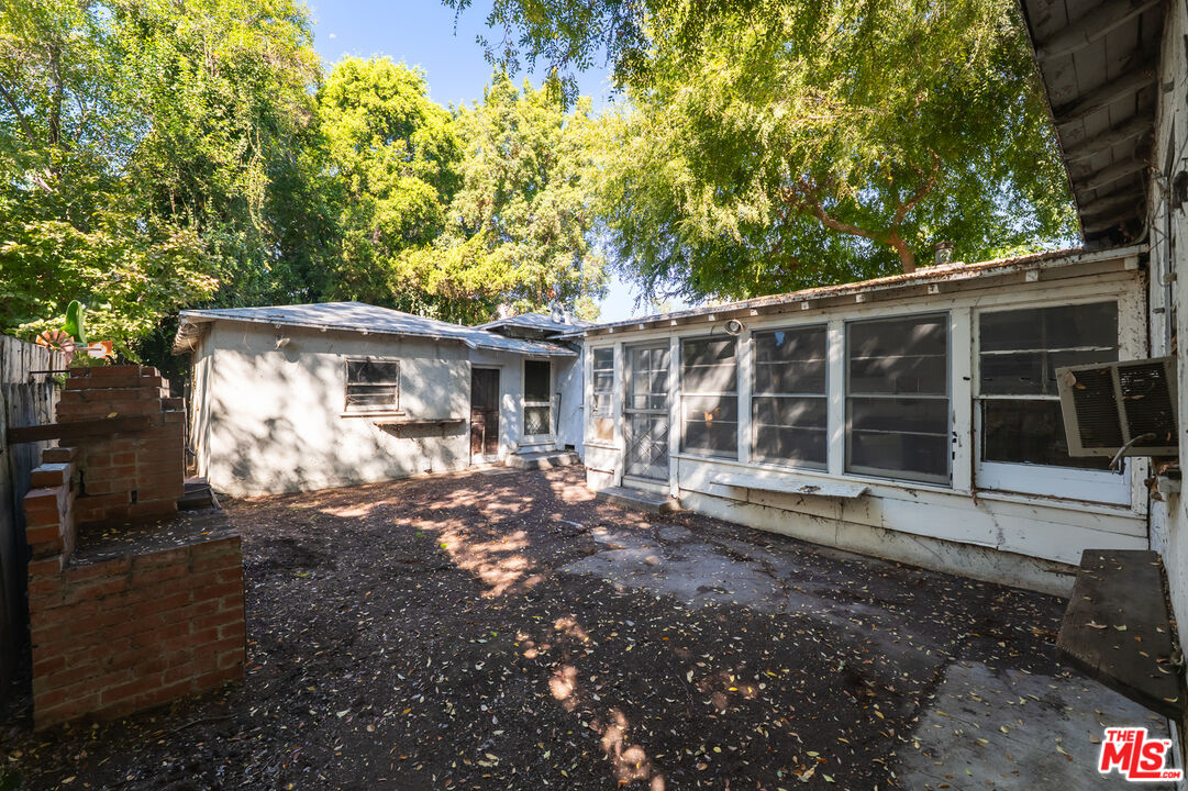 Shaded backyard patio with broad house windows, mature trees and a brick planter.