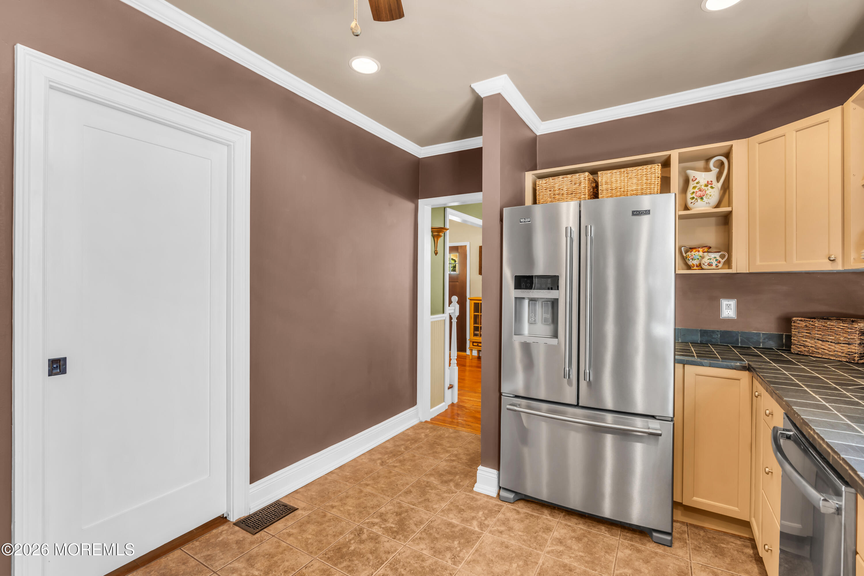 Kitchen with a stainless steel French-door refrigerator, light wood cabinets, and dark tiled countertops.