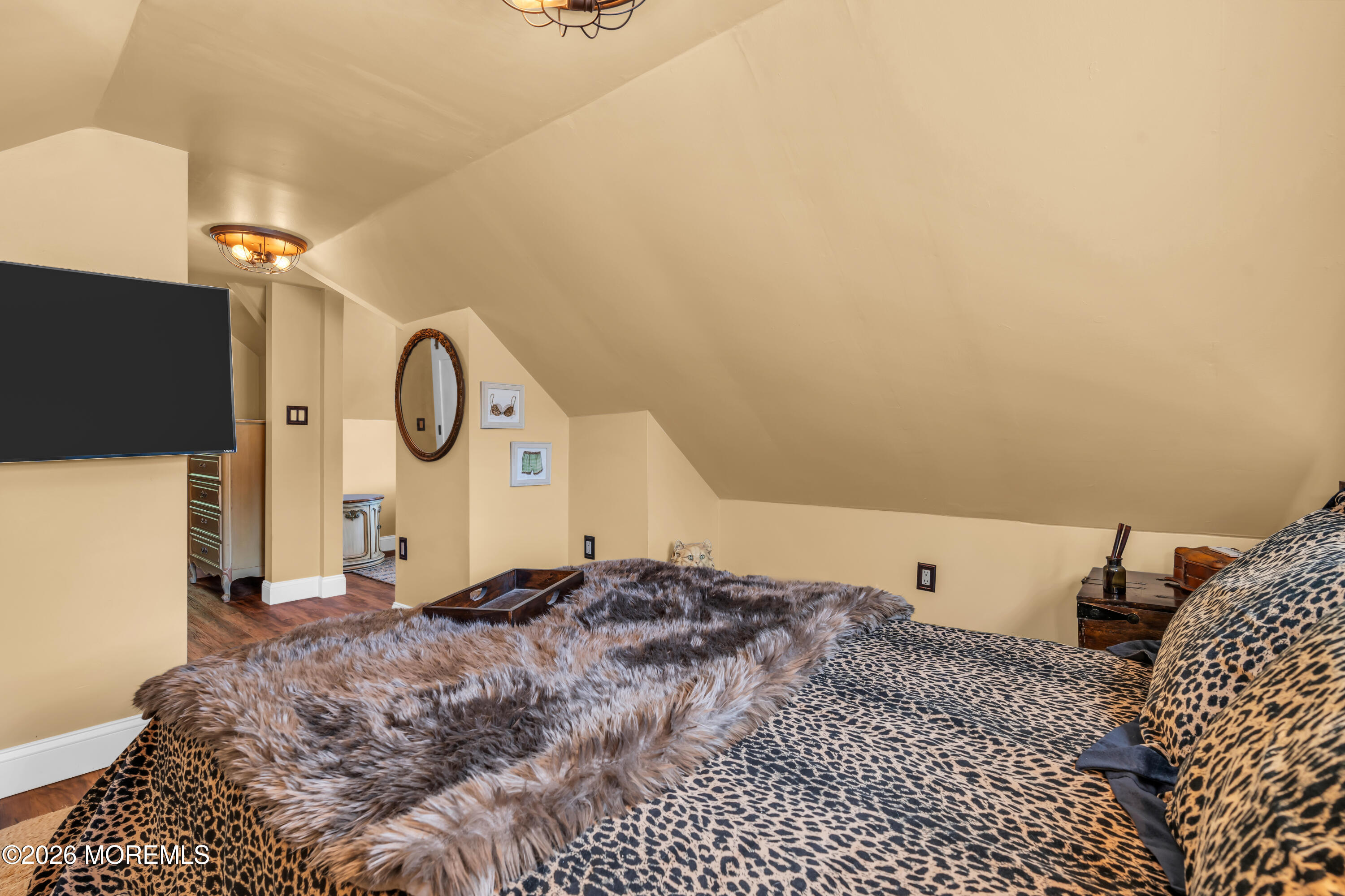 Furnished bedroom with a sloped ceiling, patterned bedding, and wall-mounted television.