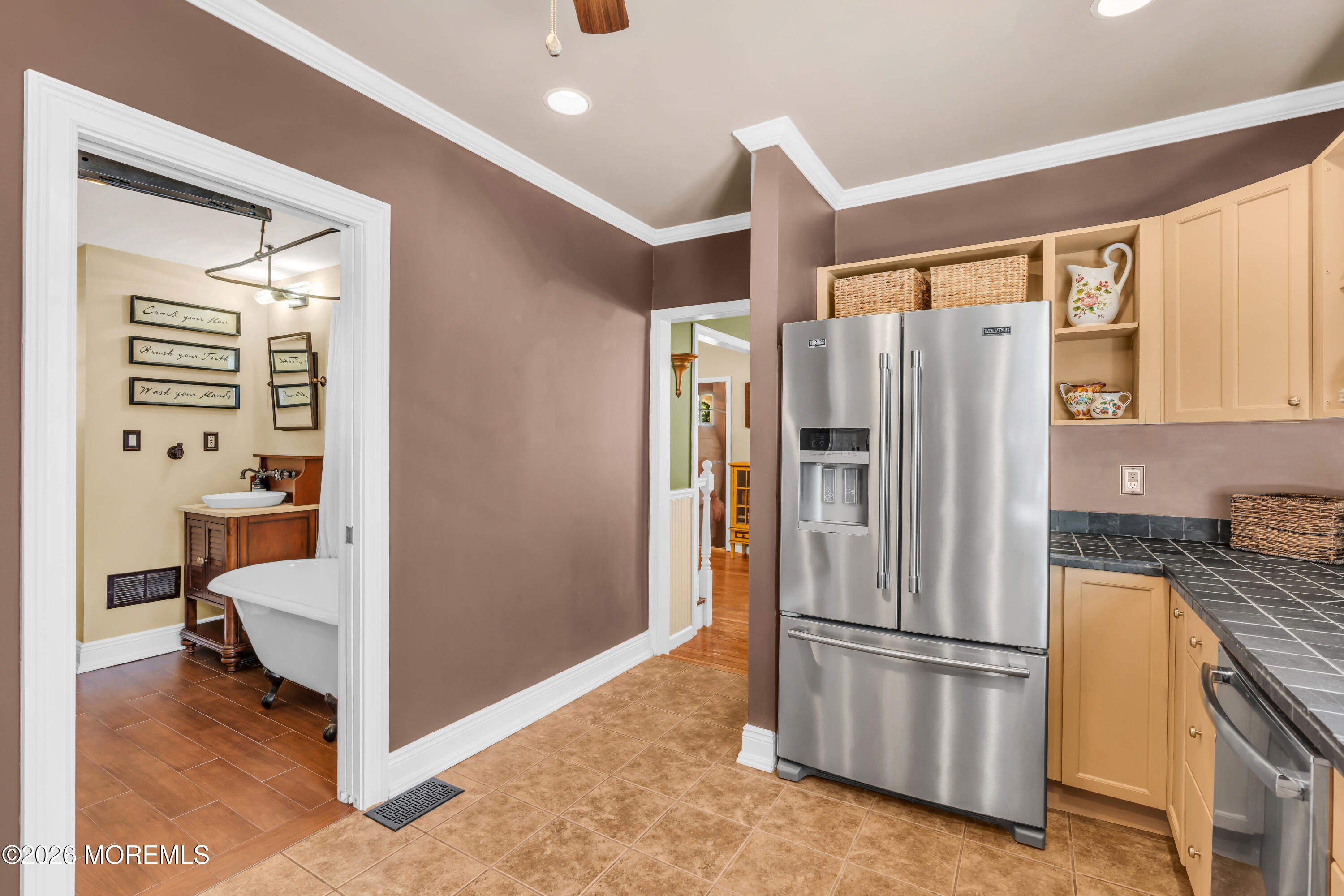 Kitchen with a stainless steel refrigerator, pale wood cabinets, and a view into the adjoining bathroom.