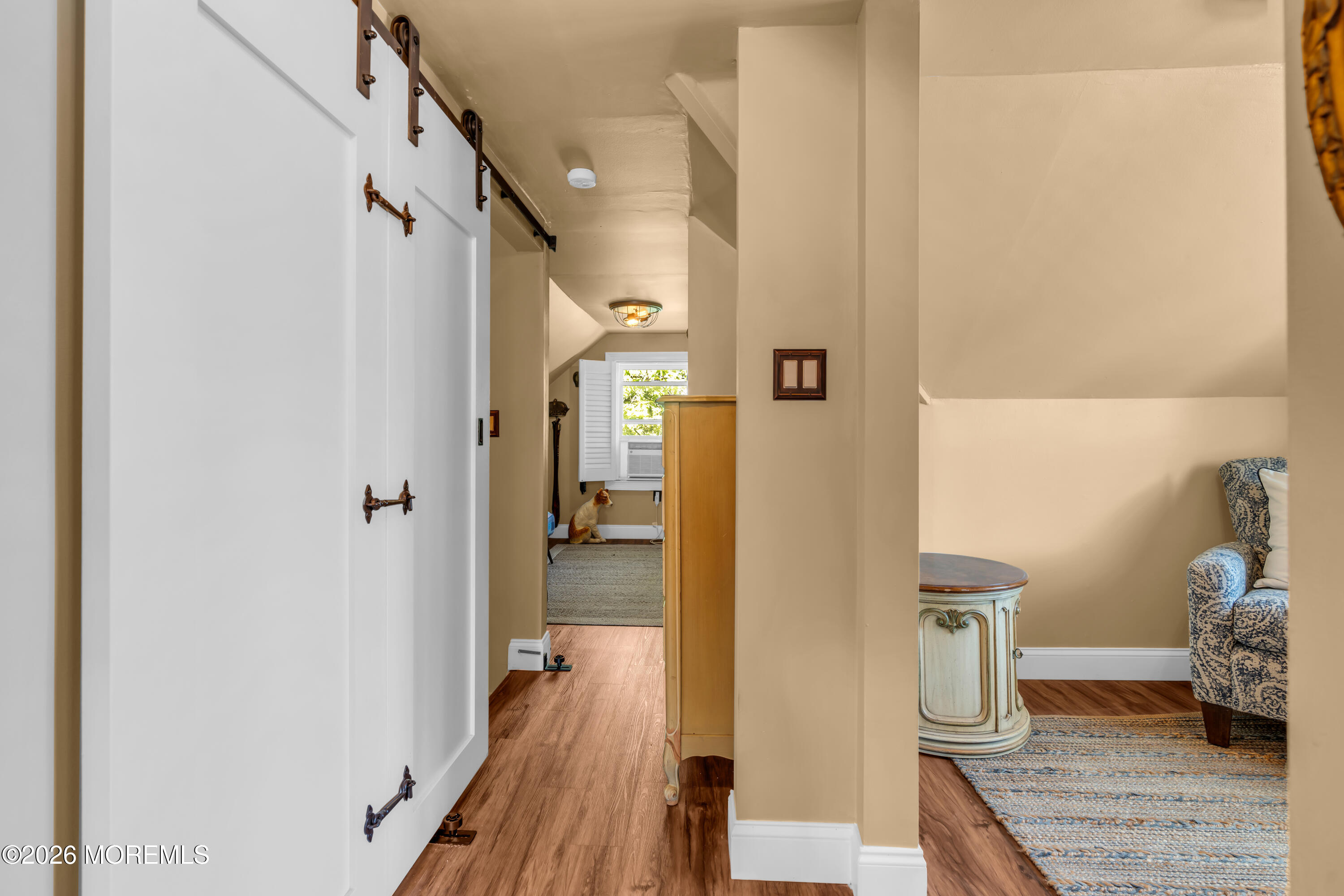 Hallway and sitting area with a white barn door and a cat by the window.