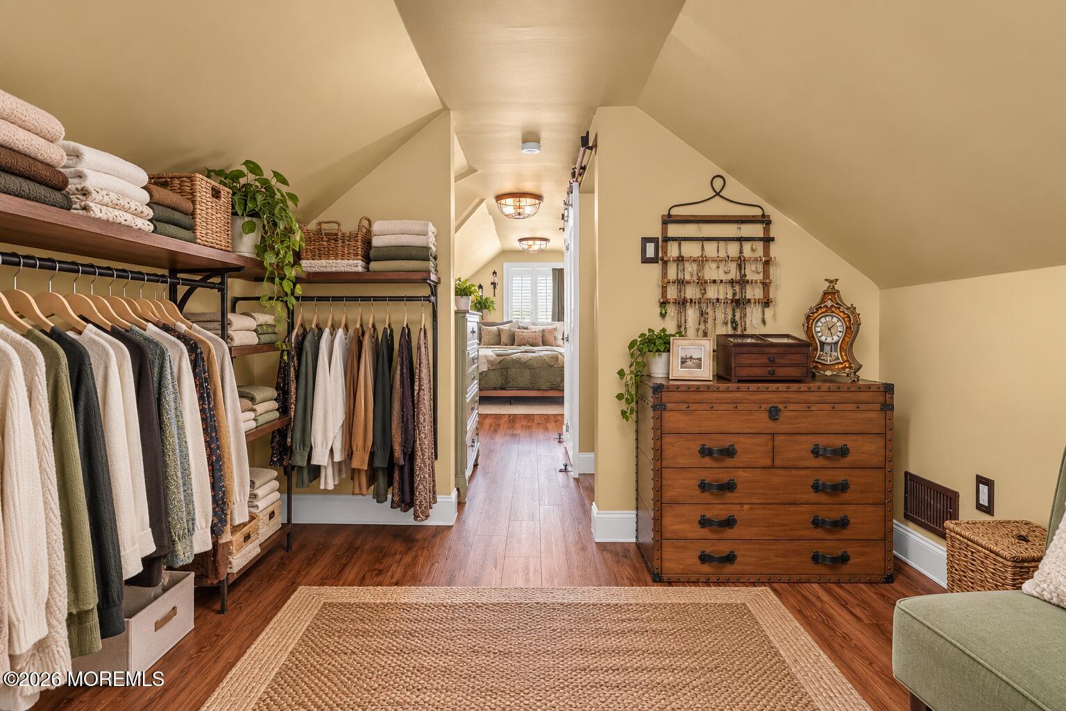 Walk-in closet with open clothing shelves, a wooden chest, and a bedroom visible through the doorway.
