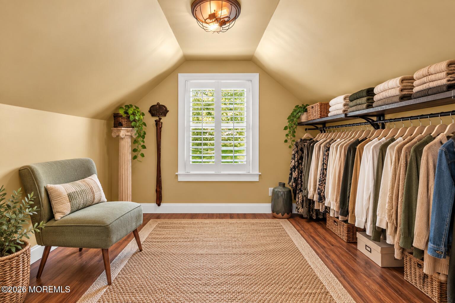 Dressing room with a clothing rail, shuttered window, upholstered chair, and woven rug.