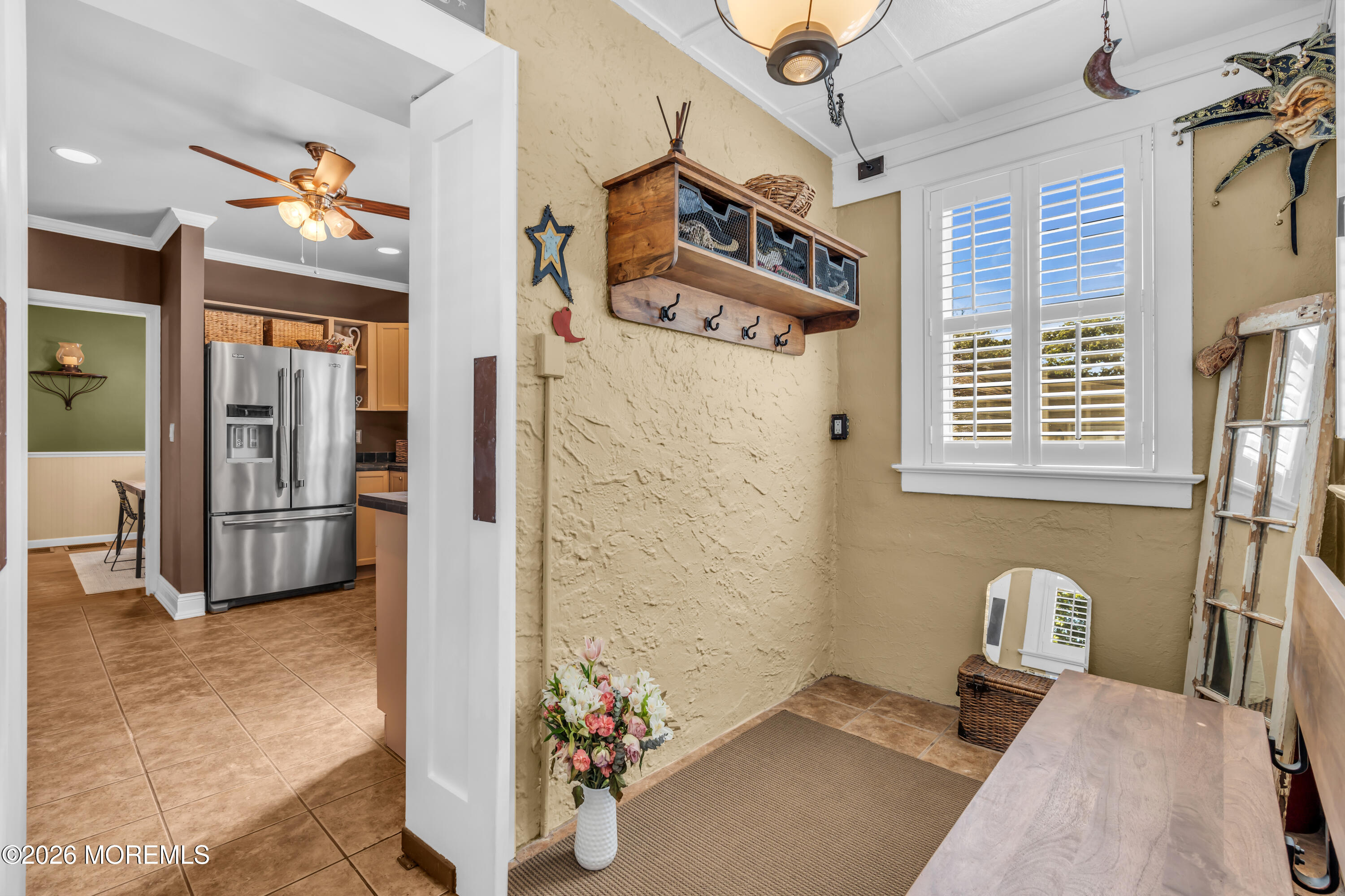 Mudroom with rustic wooden hooks, shuttered window, tiled floor, and a view into the kitchen.