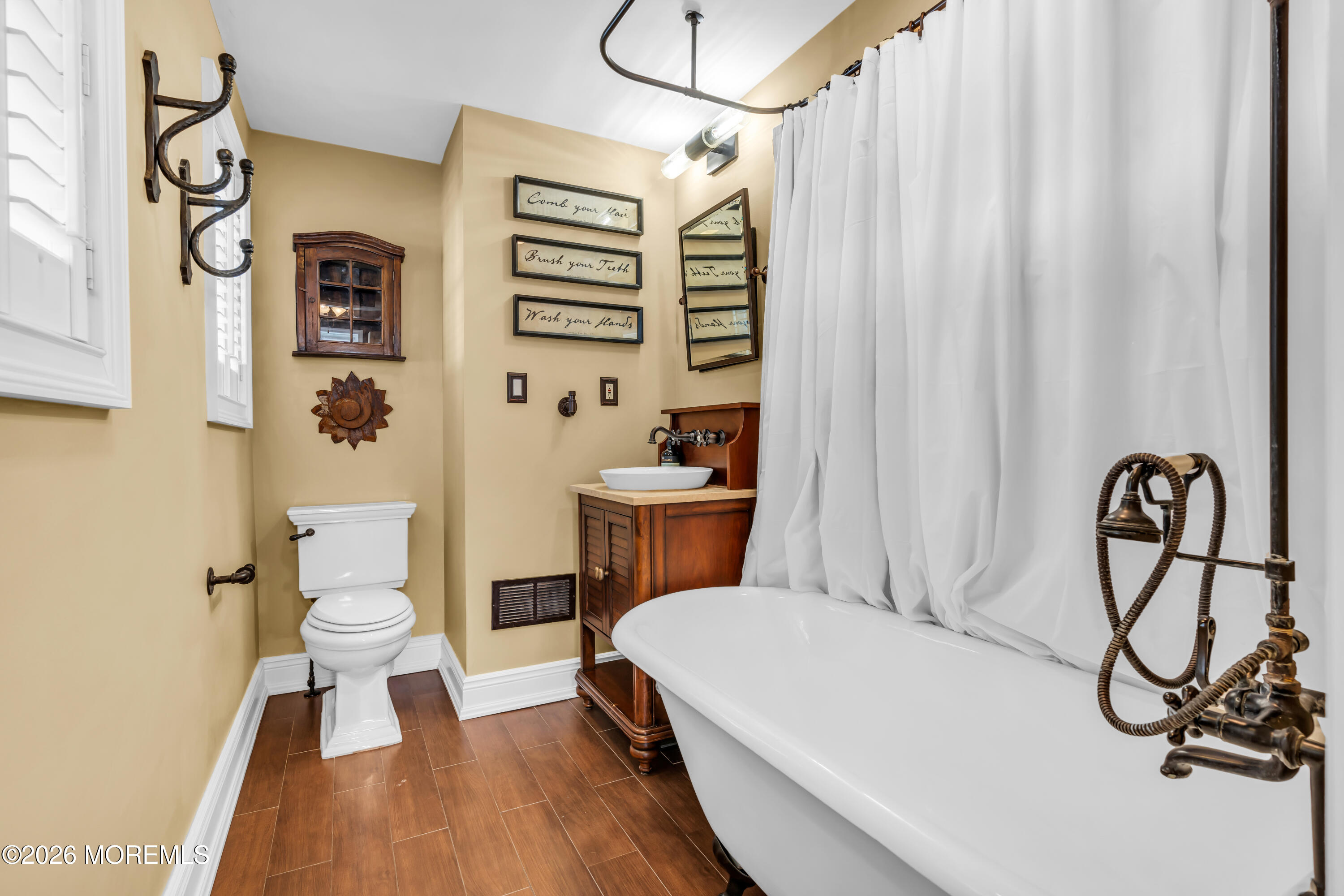 Bathroom with a white clawfoot tub, exposed bronze plumbing, and a dark wood vanity.