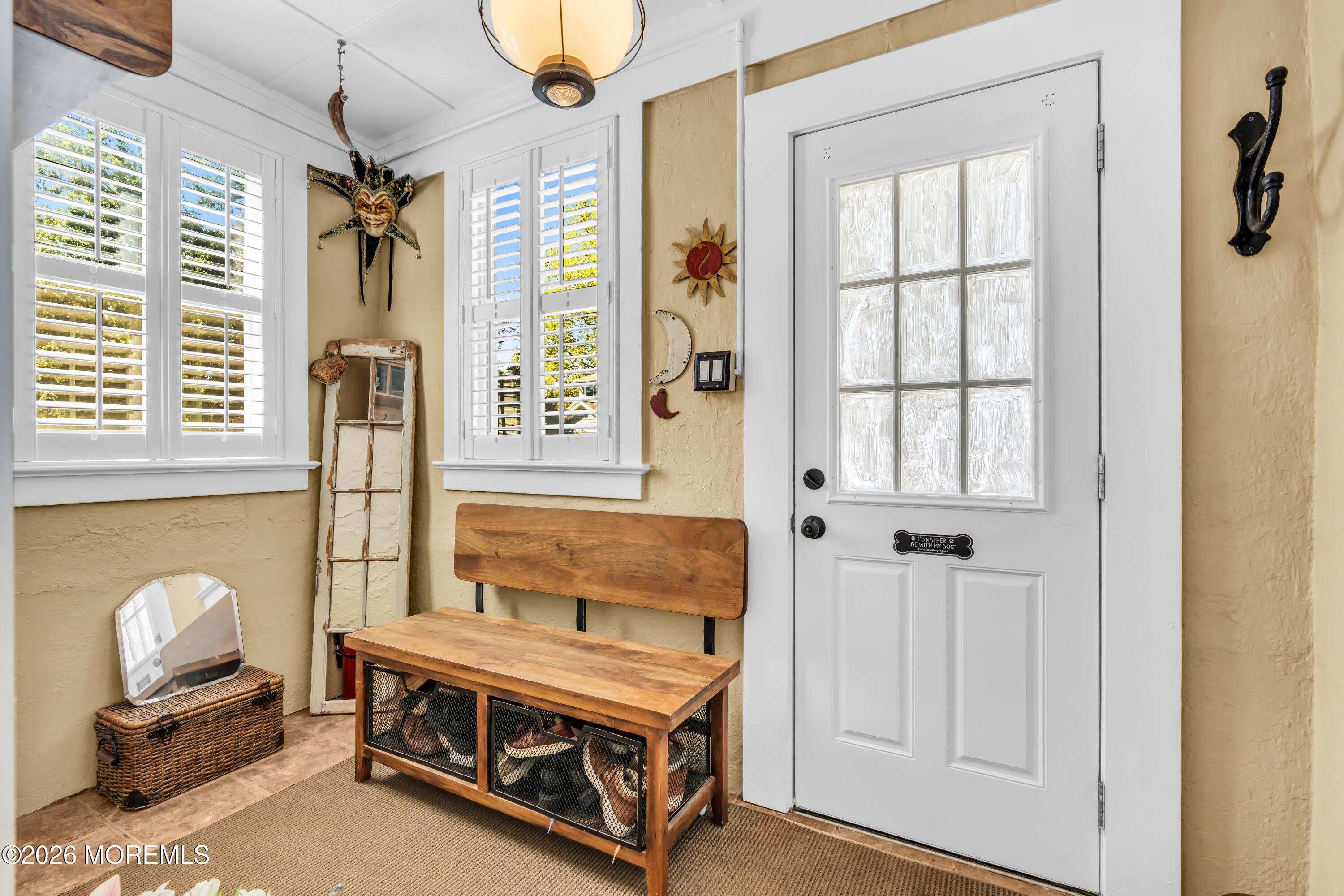 Furnished entryway with a glass-paneled front door, plantation shutters, and a wooden storage bench.