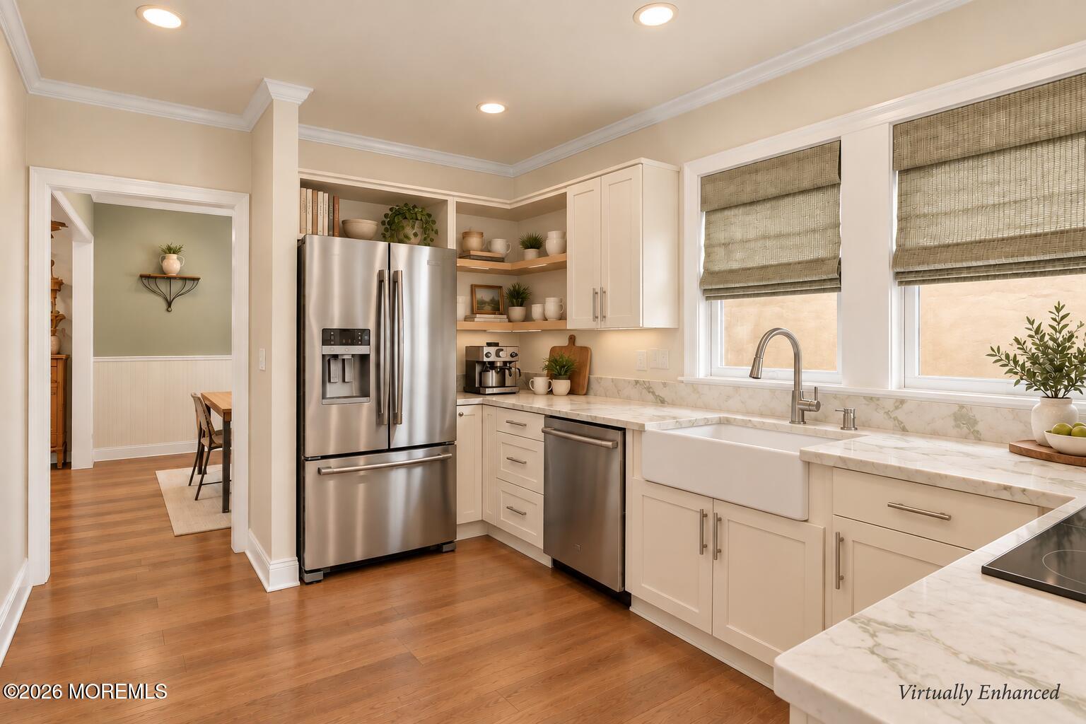 Updated kitchen with white cabinets, stainless steel appliances, farmhouse sink, and warm hardwood floors.