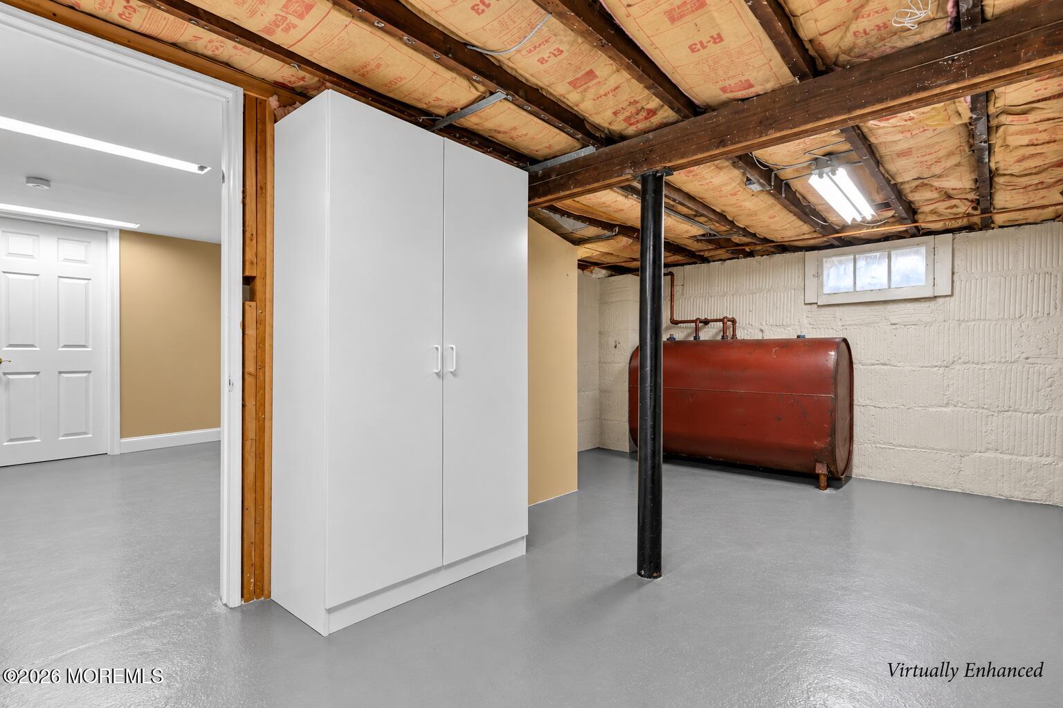 Basement utility area with a red oil tank, white storage cabinet, and exposed insulated ceiling.