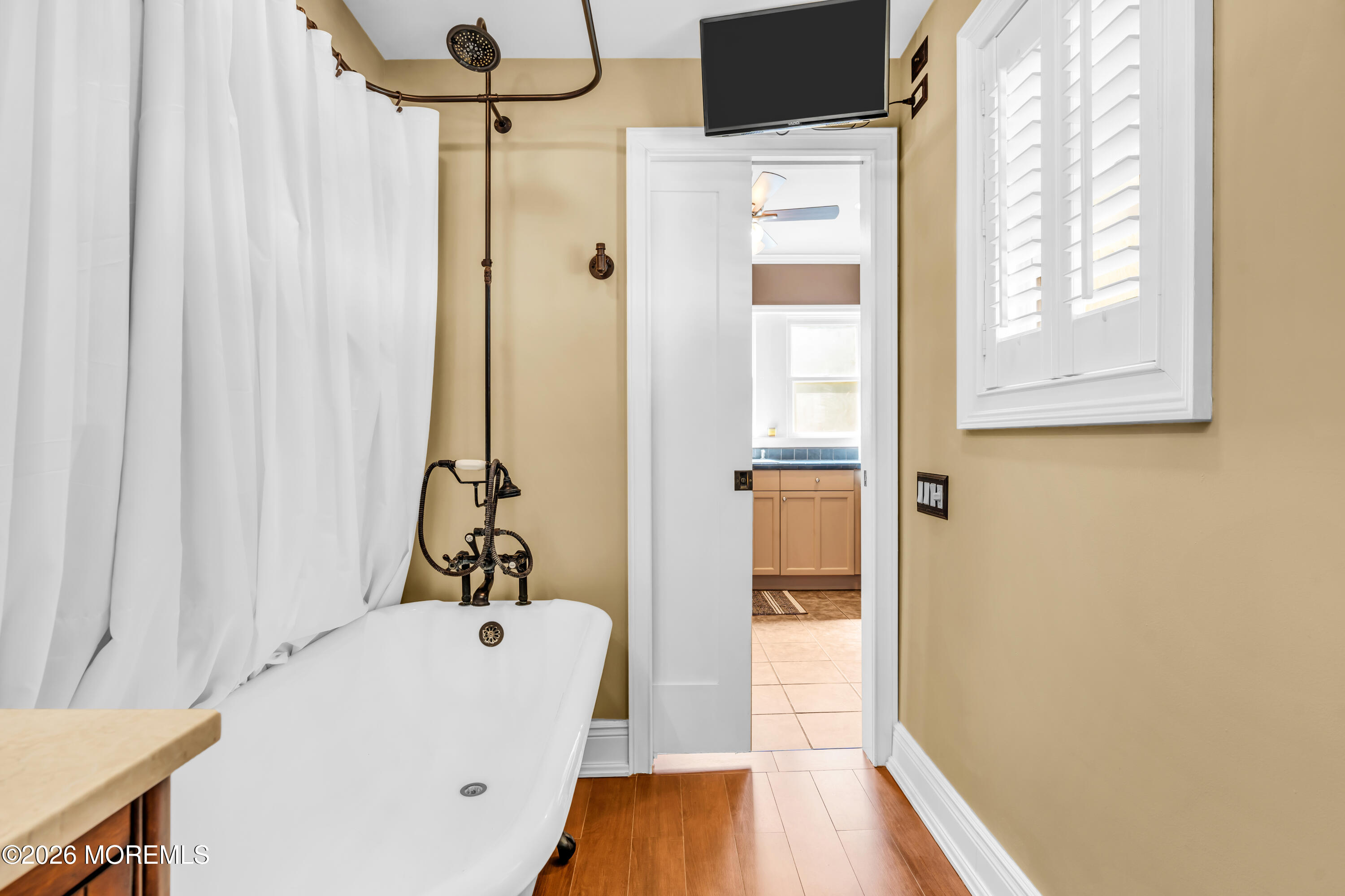 Bathroom with a clawfoot tub, bronze shower fixtures, and plantation shutters.