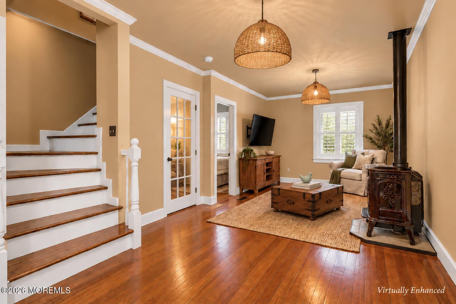 Living room with a wood-burning stove, hardwood floors, and a staircase with dark wood treads.