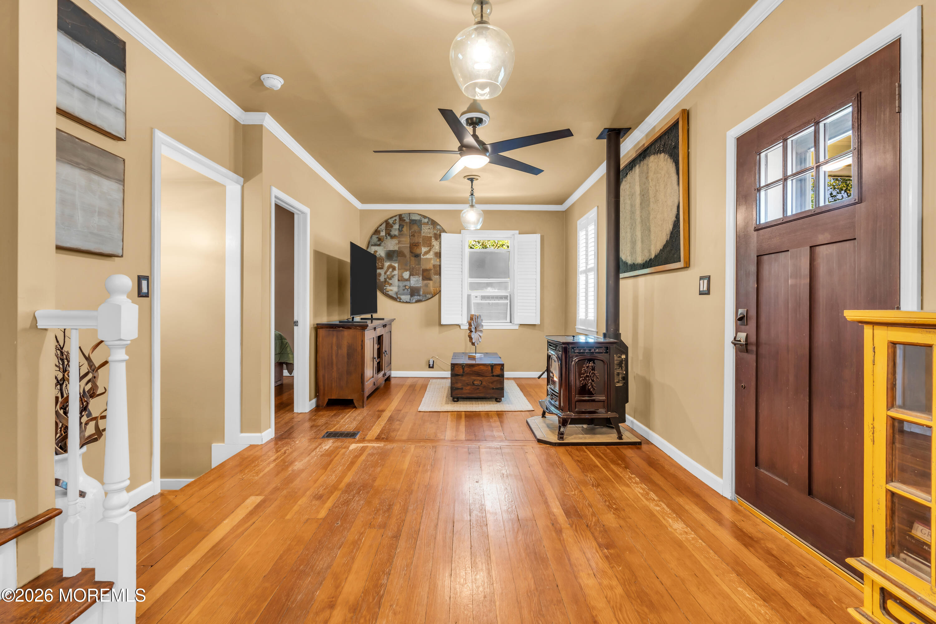 Living room with hardwood floors, a wood-burning stove, and a ceiling fan.