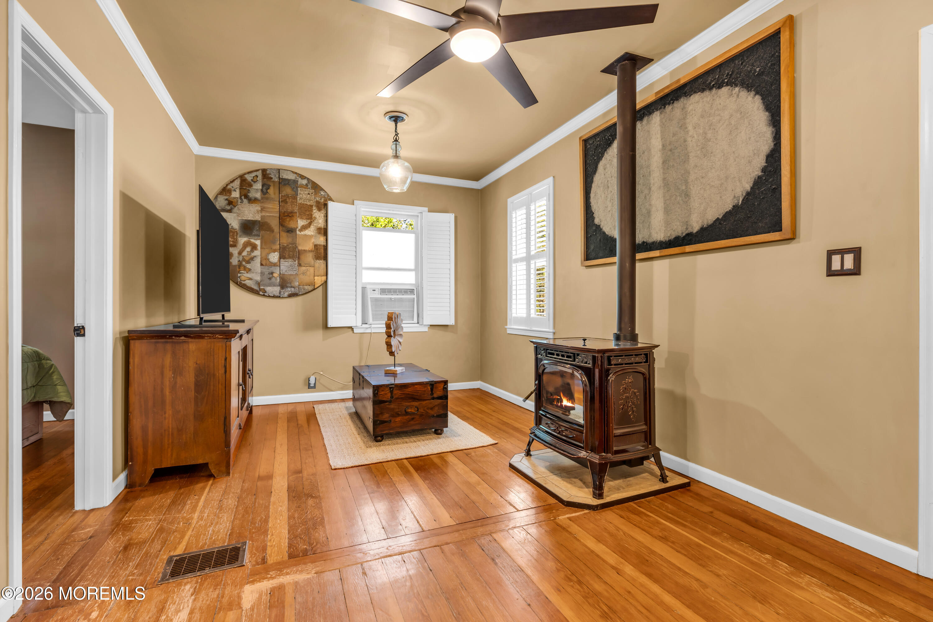 Living room with a lit wood stove, hardwood floors, and shuttered windows.