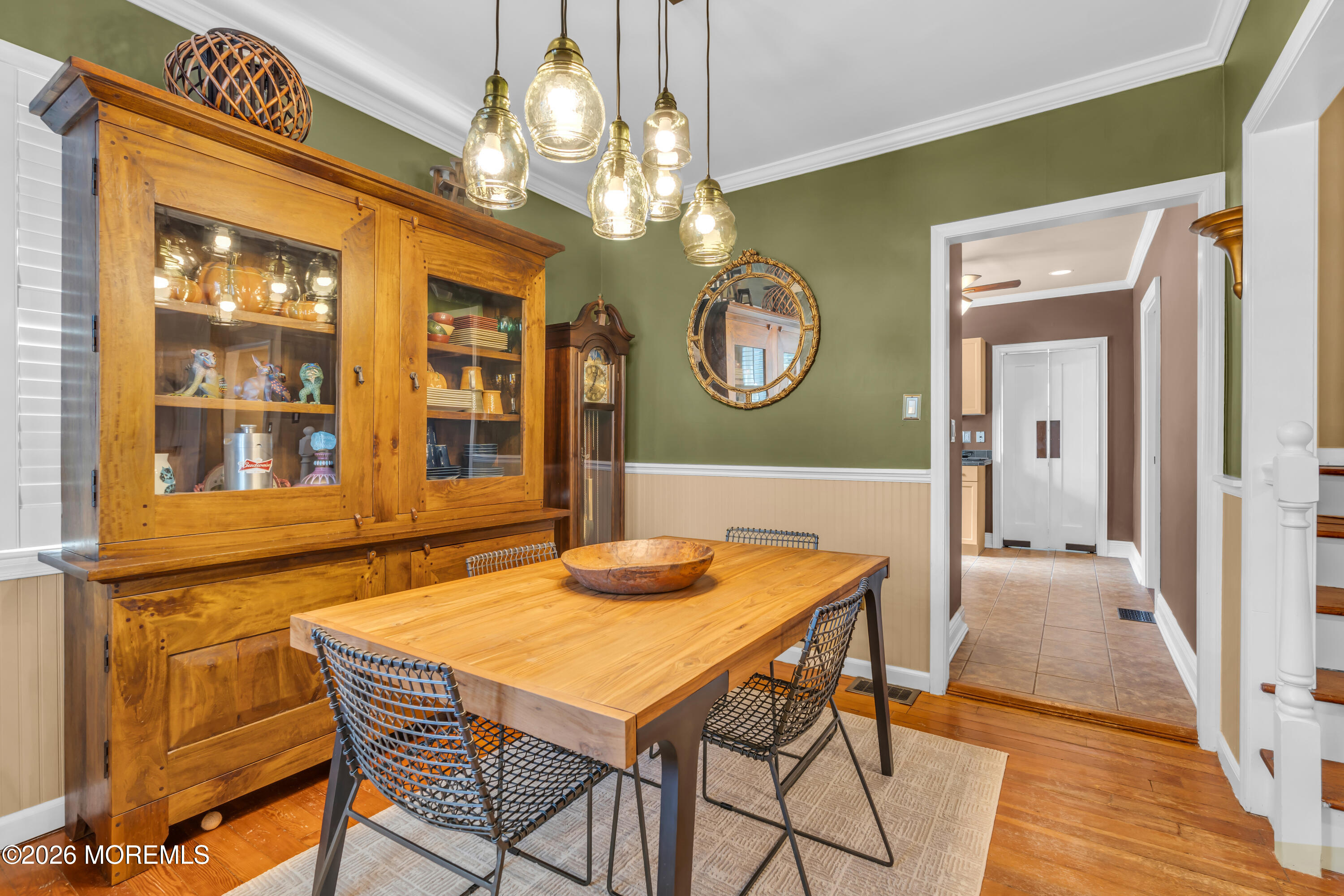 Dining room with a rustic wooden table, large display hutch, and glass pendant lights.