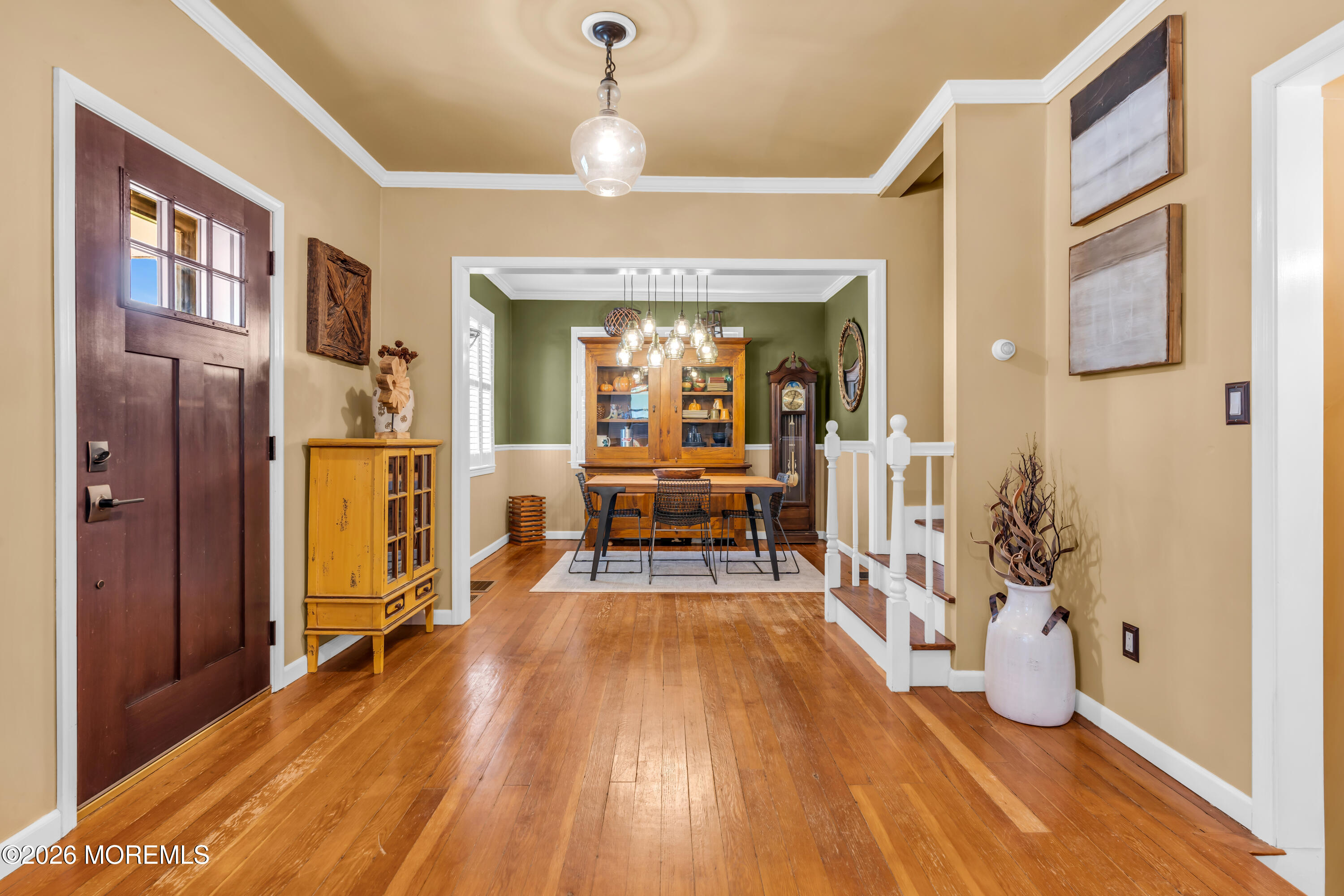Entry foyer with hardwood floors, dark wood front door, and view into a furnished dining room.