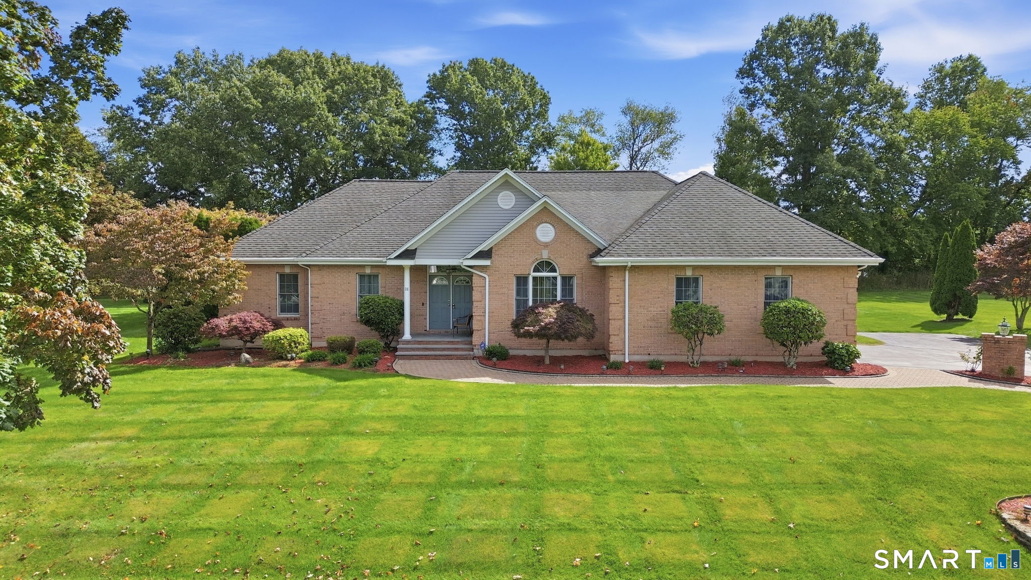 Single-story brick home with a gabled entrance, landscaped gardens, and a broad green lawn.