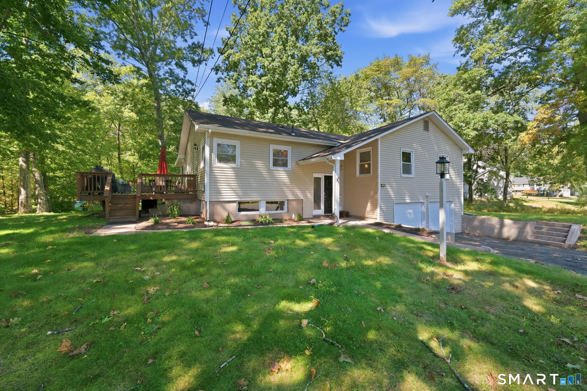 Split-level home with attached garage and raised deck, set among mature trees and a grassy yard.