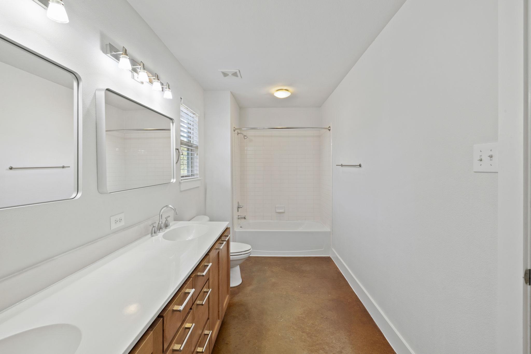 Bathroom with a long white vanity, wood cabinets, and a tiled tub and shower.