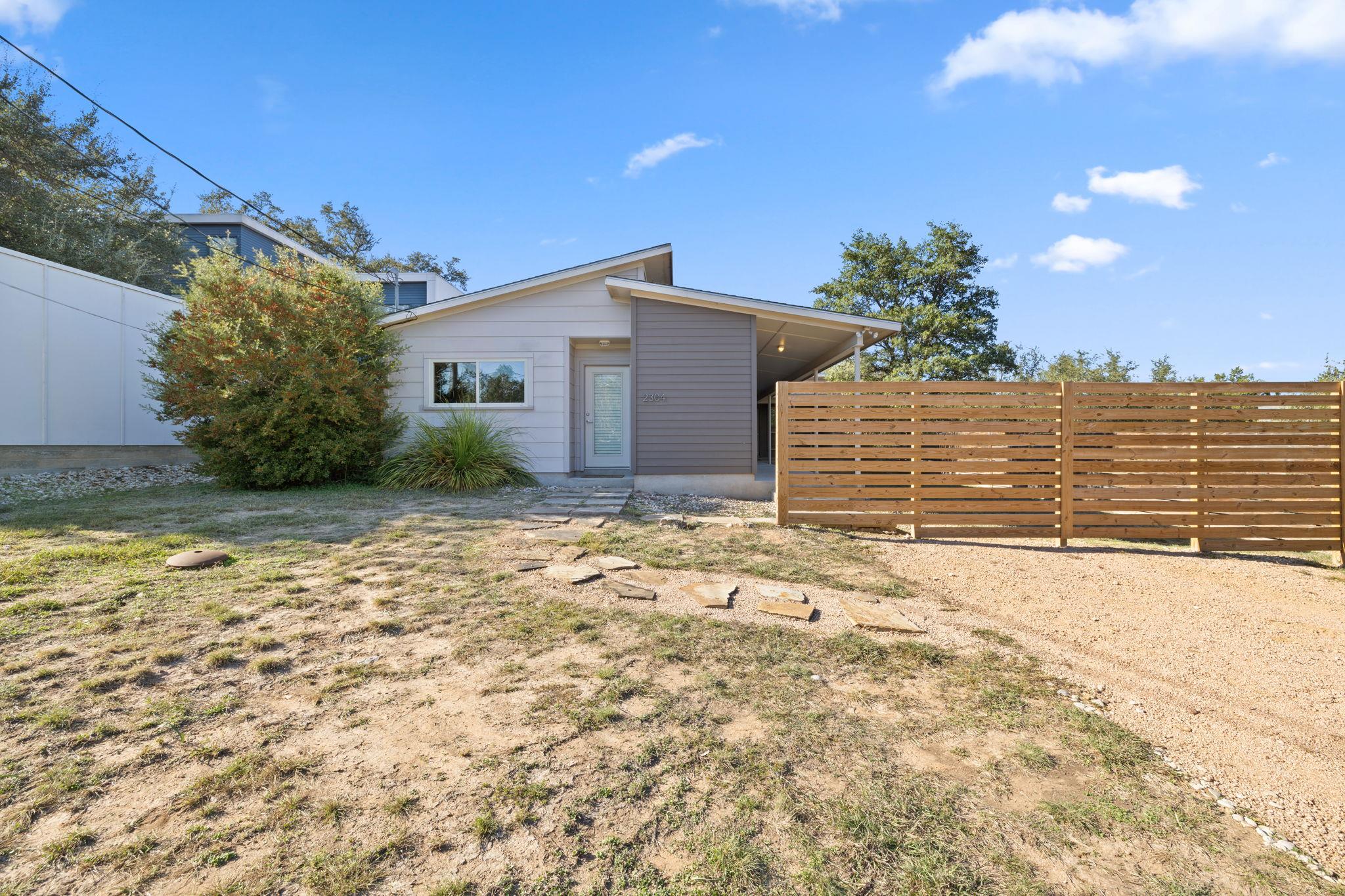 Modern gray home with a covered entry, stepping-stone path, and horizontal wood fence.