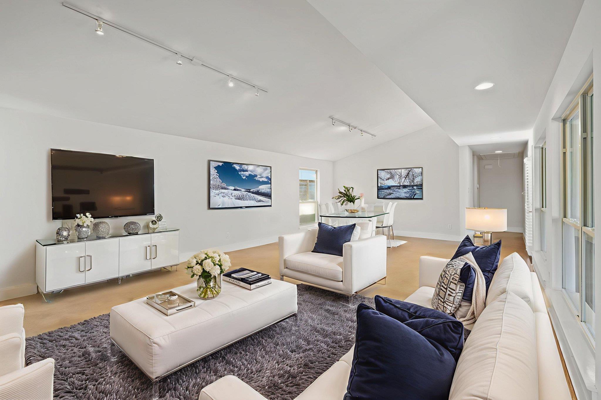 Open-plan living room with white seating, navy cushions, floor-to-ceiling windows, and dining area.