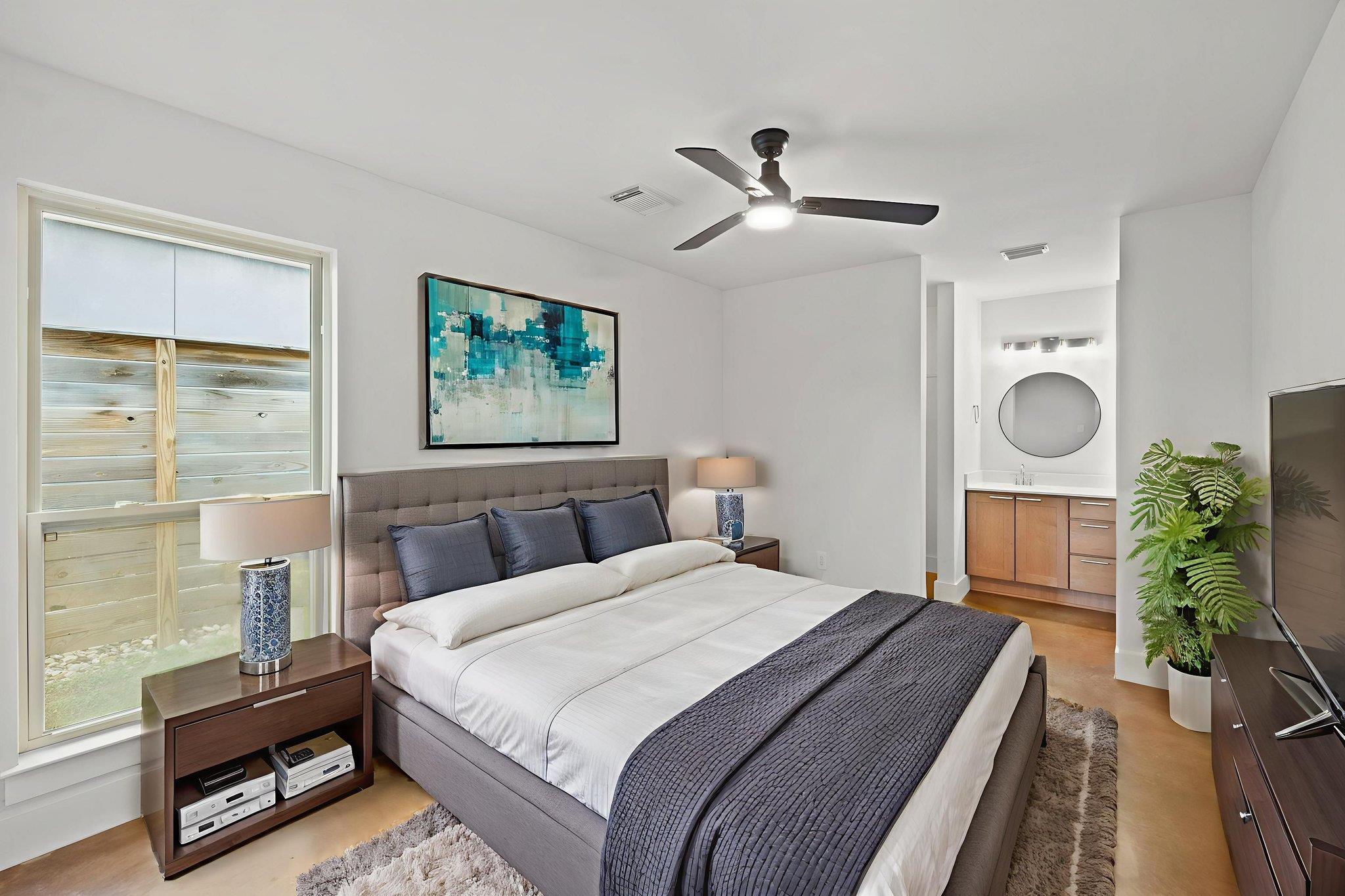 Furnished bedroom with a large gray-upholstered bed, teal artwork, and an en suite vanity.