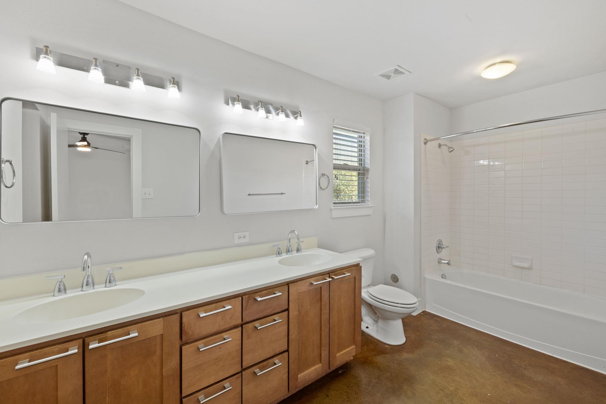 Bathroom with a long double vanity, two mirrors, and a white-tiled tub and shower.