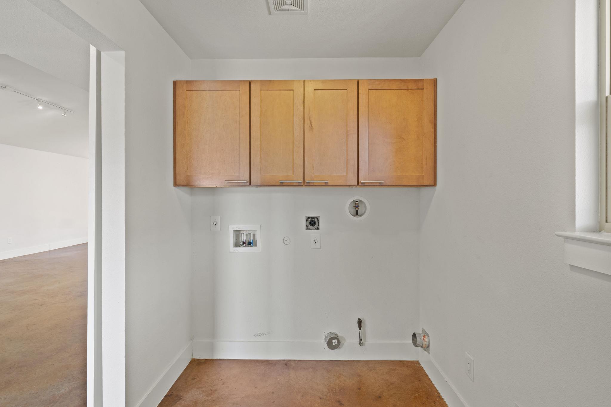 Empty laundry area with wood cabinets, exposed washer and dryer hookups, and a window.