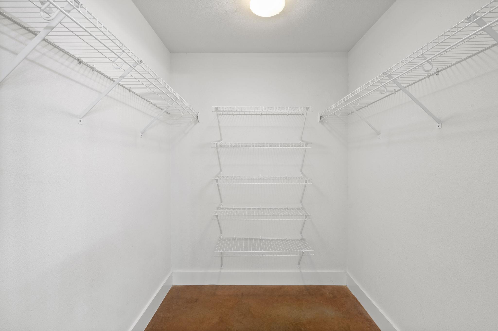 Empty walk-in closet with white wire shelving on three walls and a brown floor.