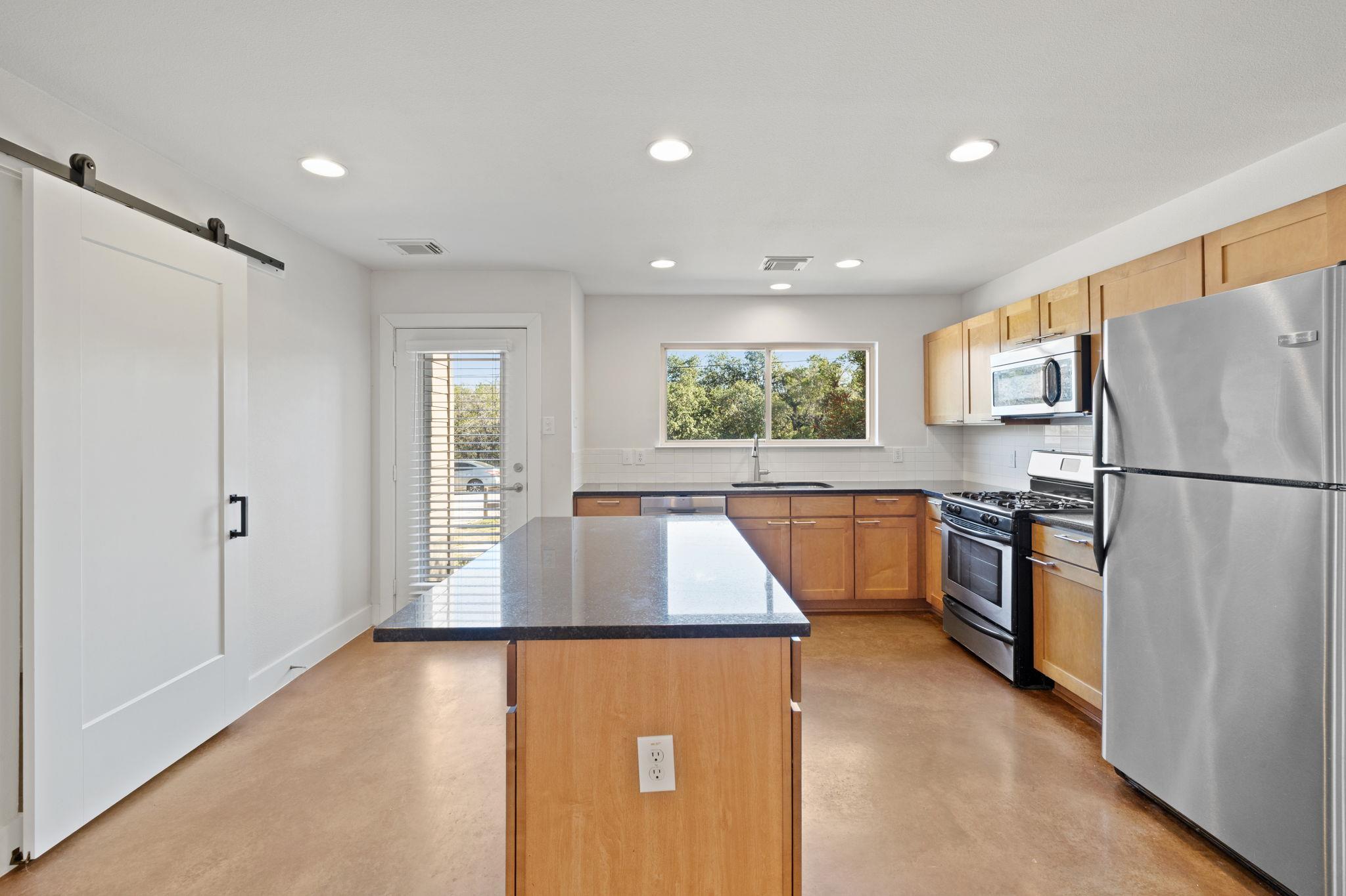 Kitchen with a large dark-countertop island, warm wood cabinets, and stainless steel appliances.