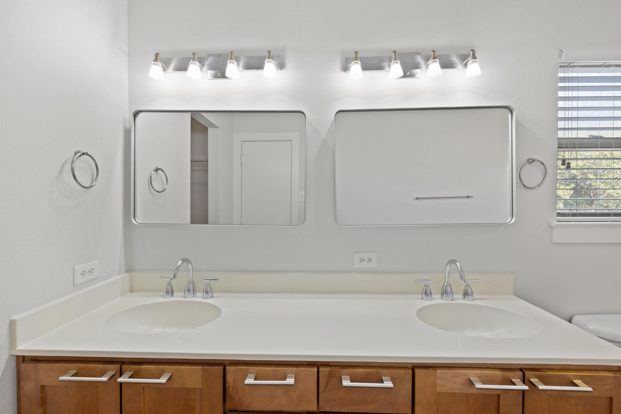 Bathroom double vanity with two mirrors, chrome faucets, and warm wood cabinetry.