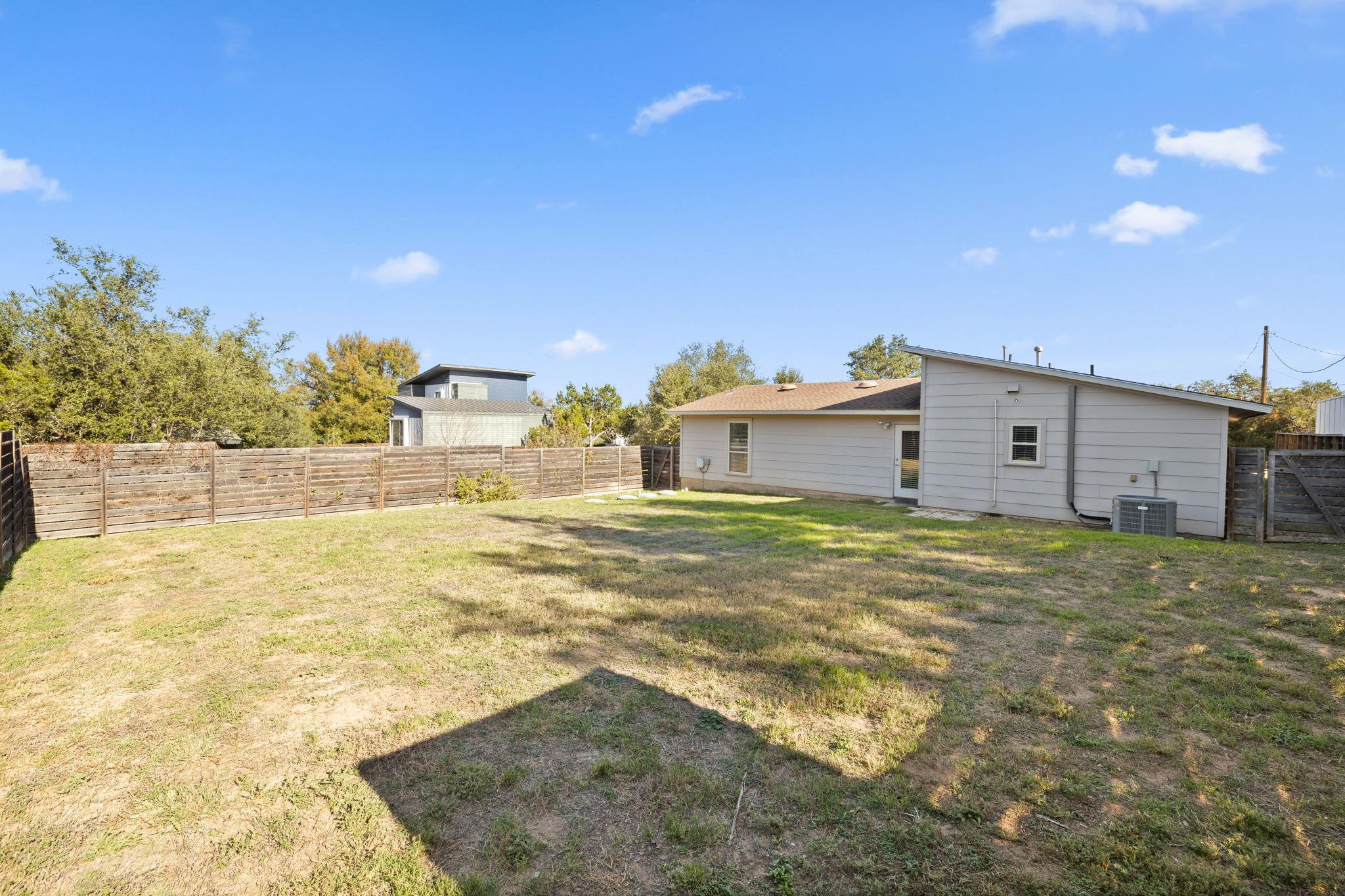 Gray house and fenced backyard with a broad, patchy lawn.