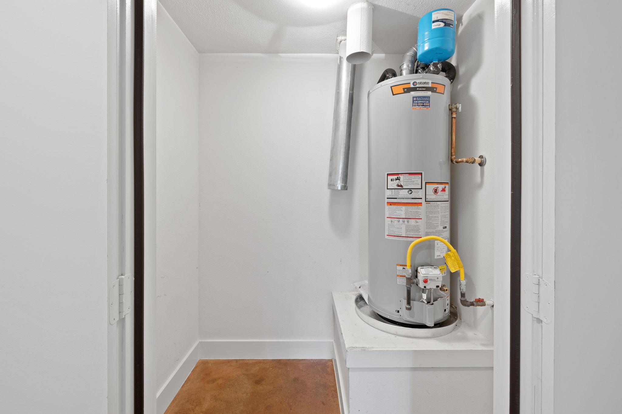 Utility closet with a gray tank water heater, blue expansion tank, and exposed plumbing.