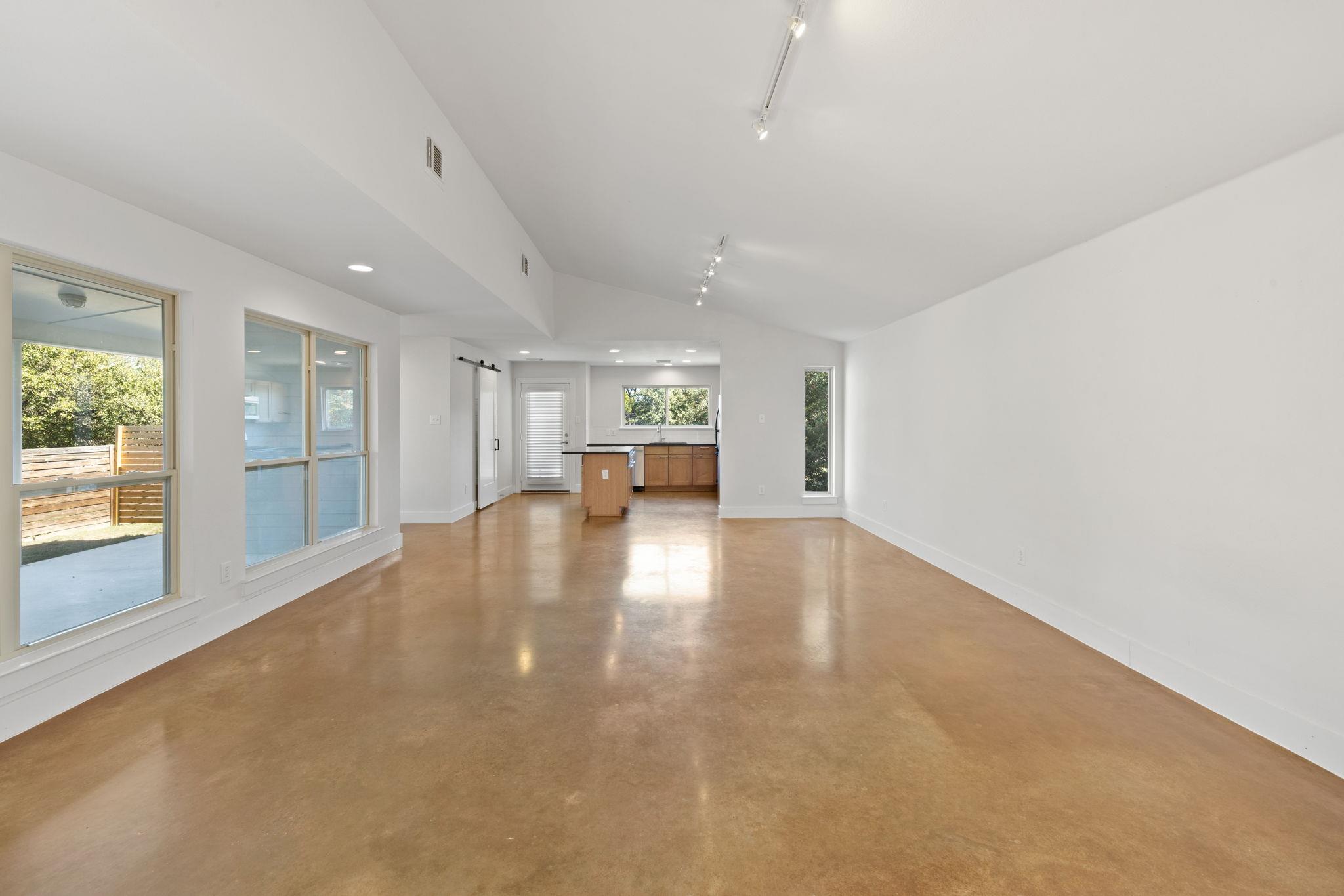 Open living room and kitchen with polished concrete floors, high ceiling, and large windows.
