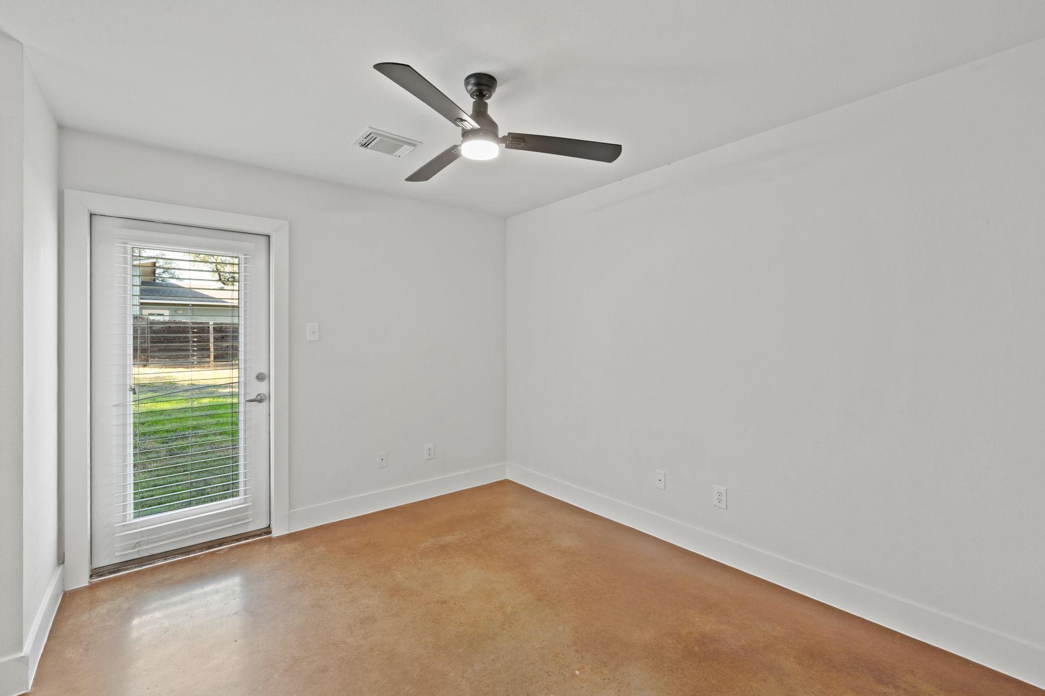 Empty room with a brown concrete floor, ceiling fan, and glass door with blinds.