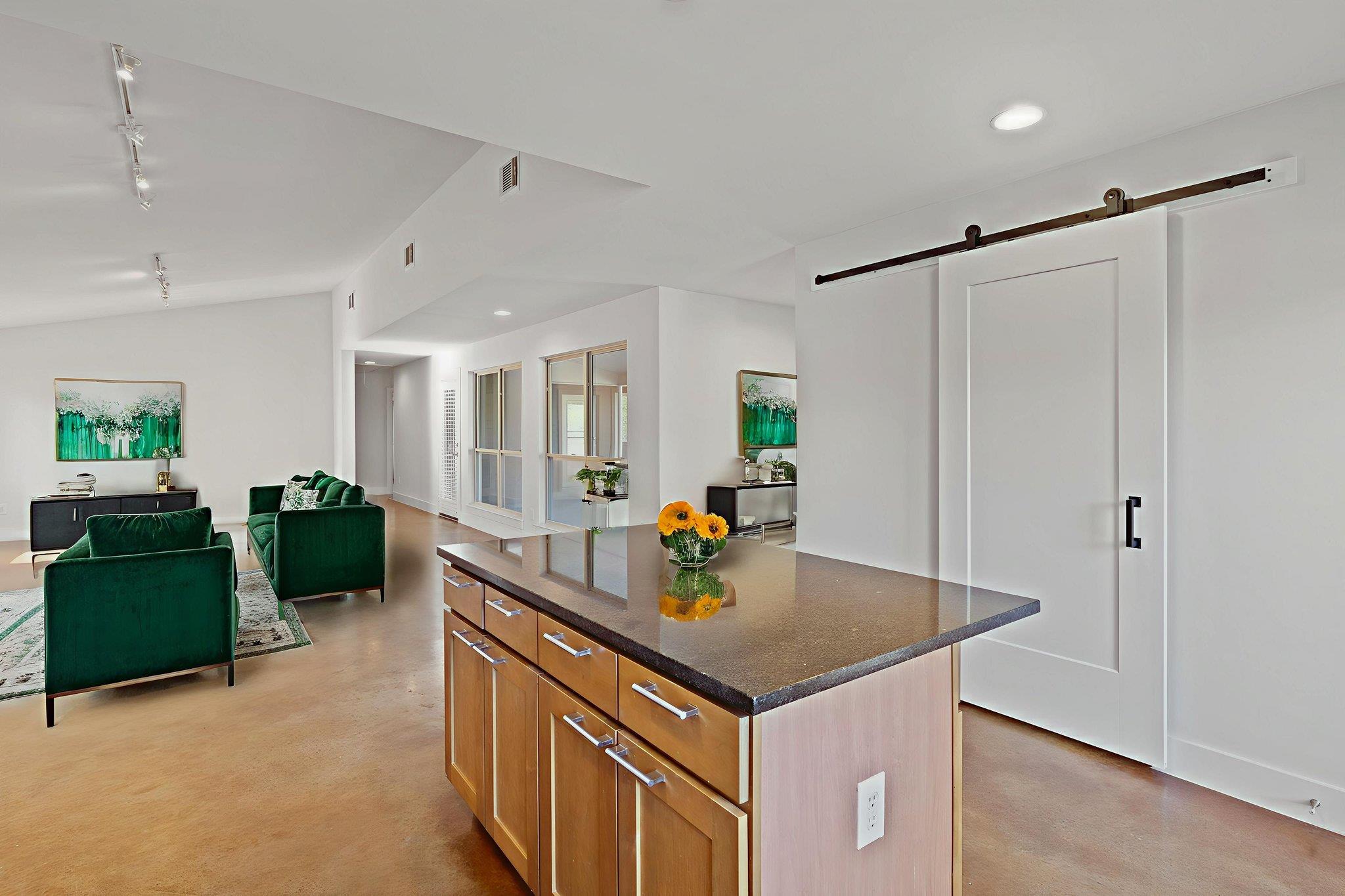 Open-plan living room and kitchen with a wood island, green sofas, and a sliding barn door.