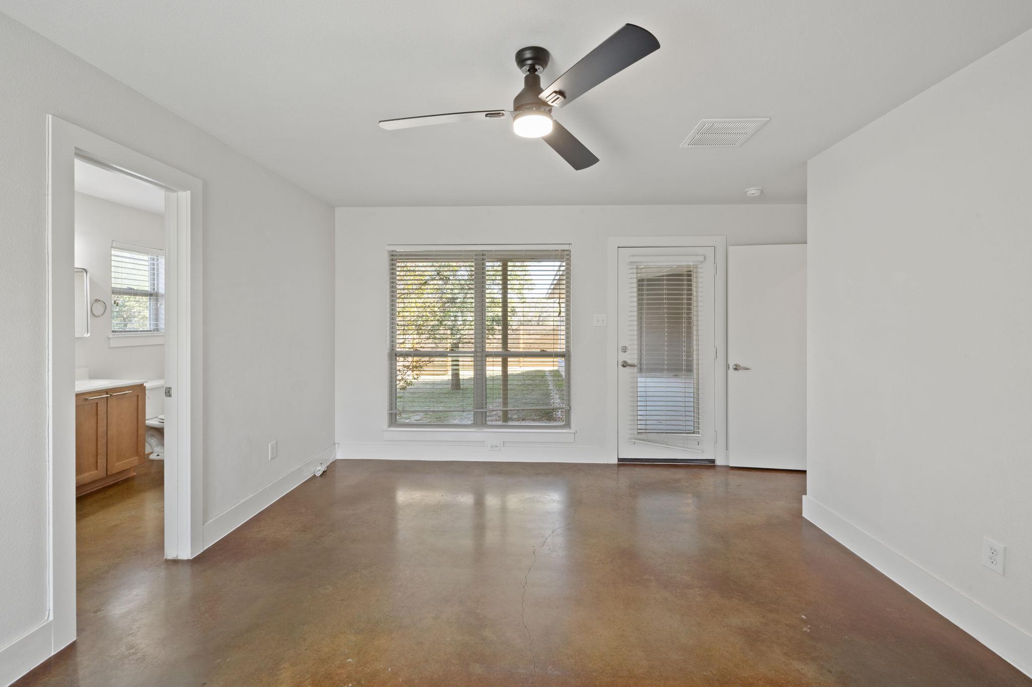 Vacant room with polished concrete floor, ceiling fan, large window, and glass-paneled door.