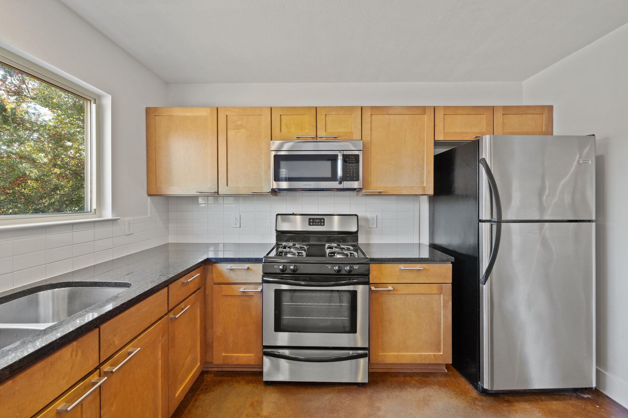 Kitchen with honey-colored cabinets, stainless-steel appliances, gas range, and a large window above the sink.