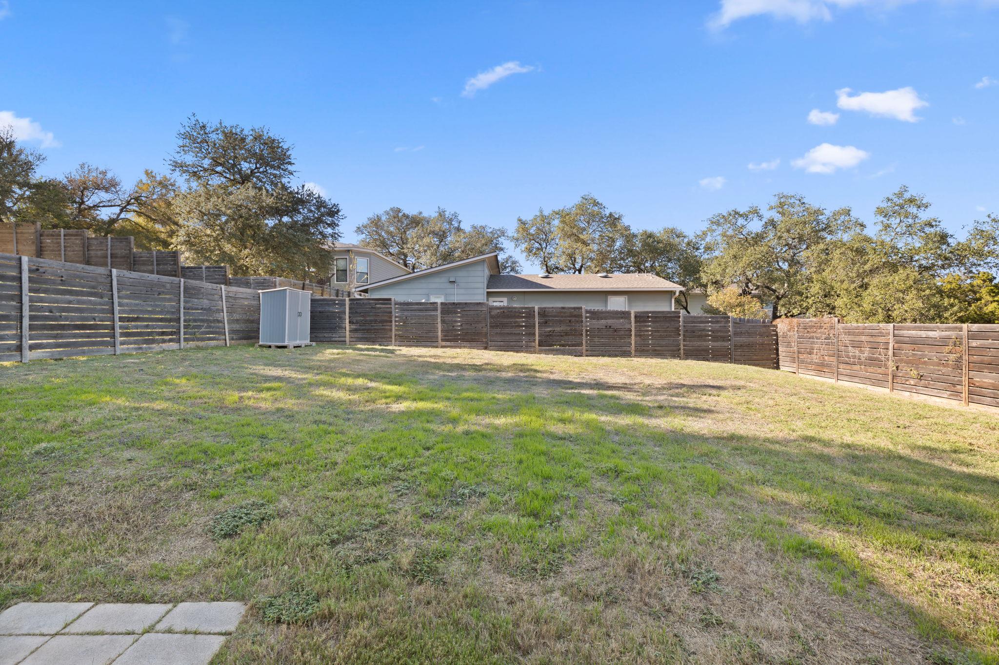 Backyard with a tall wooden fence, patchy lawn, and small storage shed.