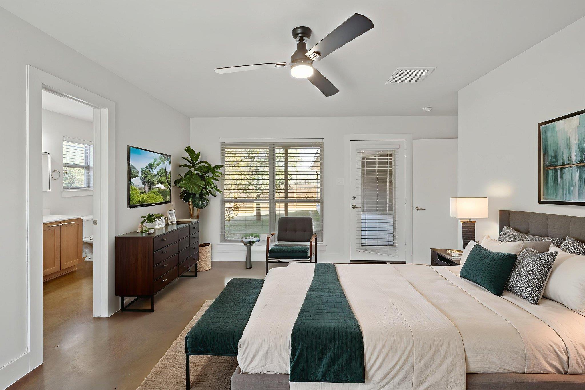 Furnished bedroom with white and teal bedding, a ceiling fan, and a bathroom visible through the doorway.