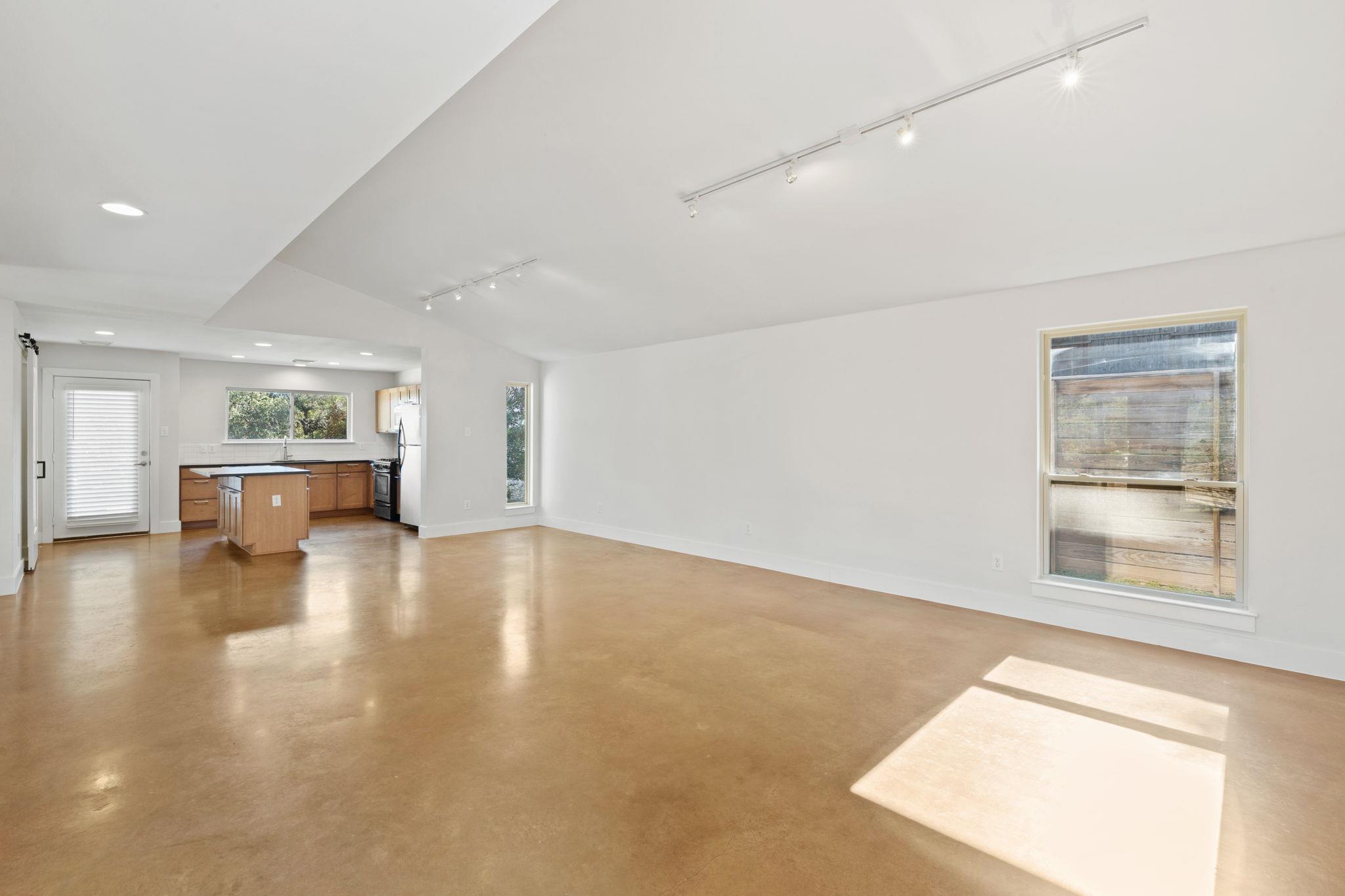 Open living room and kitchen with polished concrete floors, a wood island, and large windows.