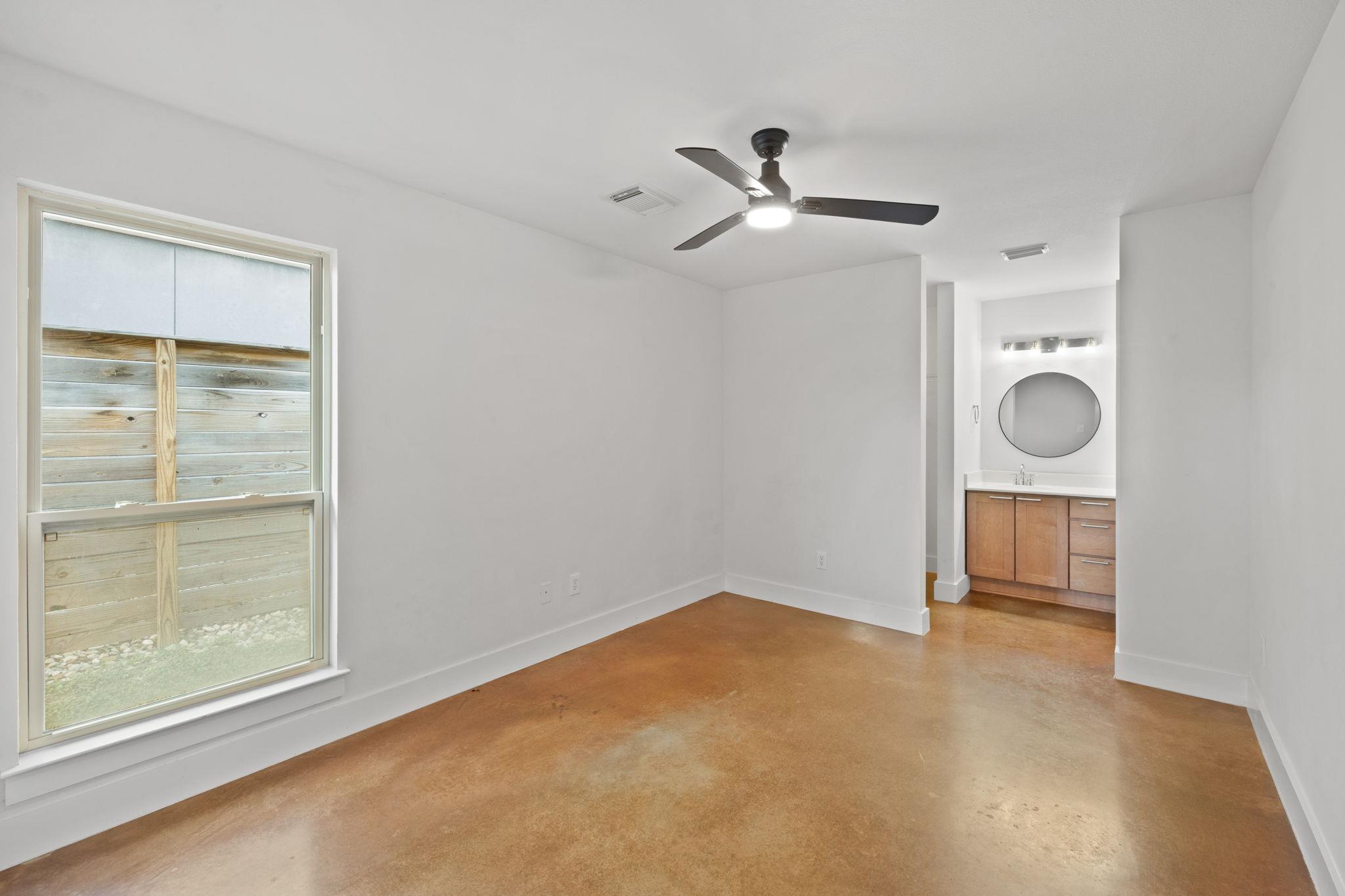 Empty room with cork flooring, a large window, ceiling fan, and adjoining vanity area.