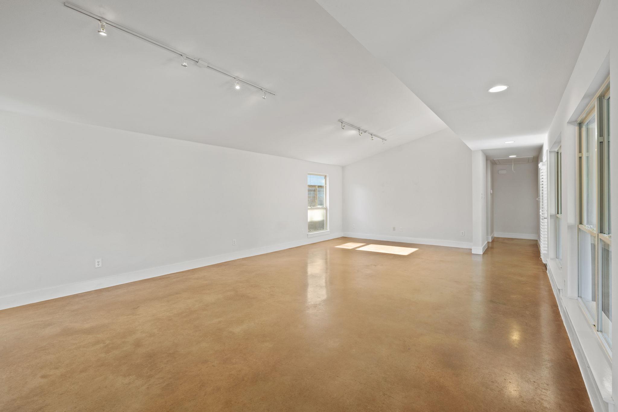 Vacant room with tan concrete floors, track lighting, and tall windows along one wall.