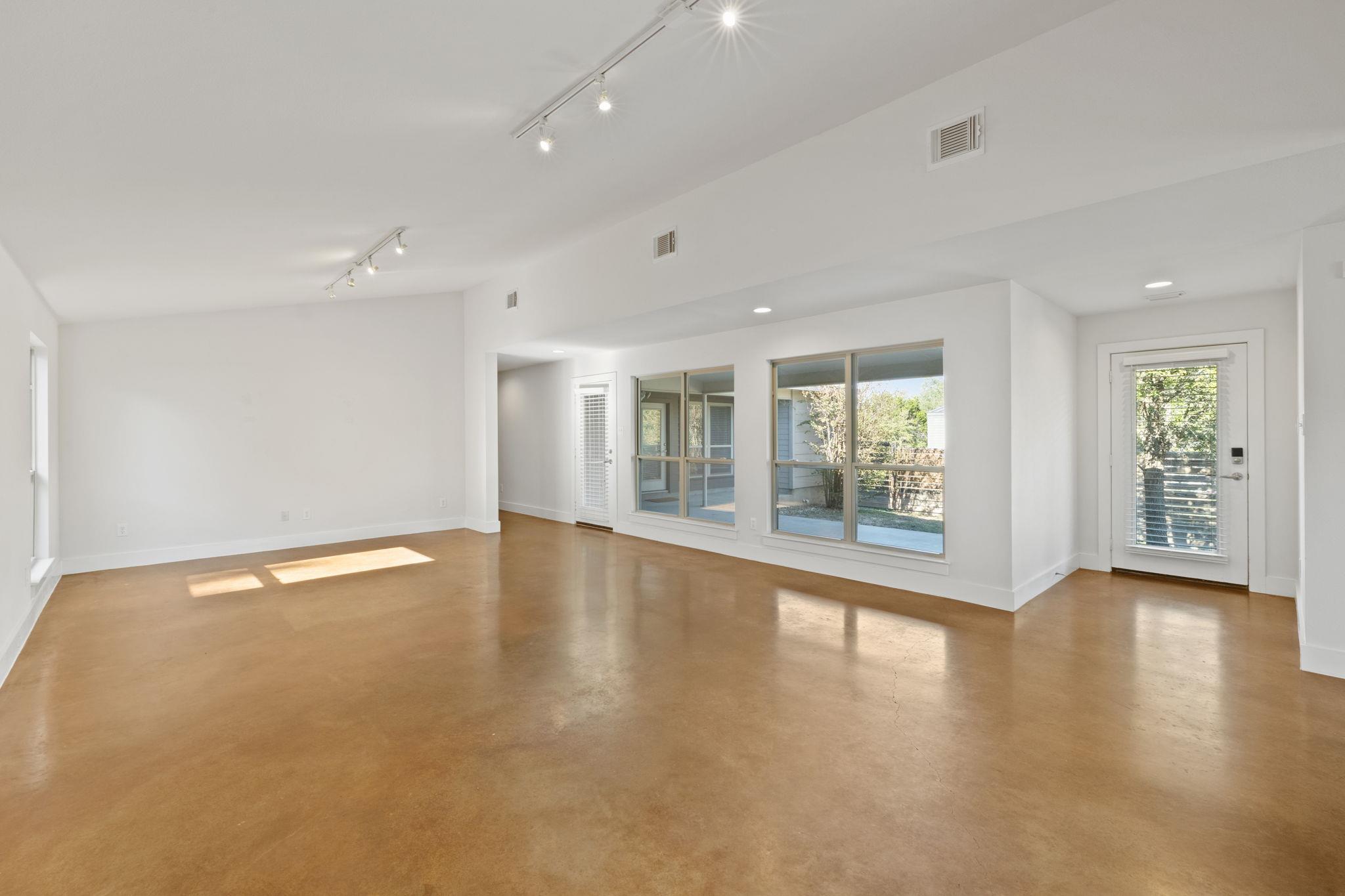 Vacant living room with warm concrete floors and large windows overlooking the yard.