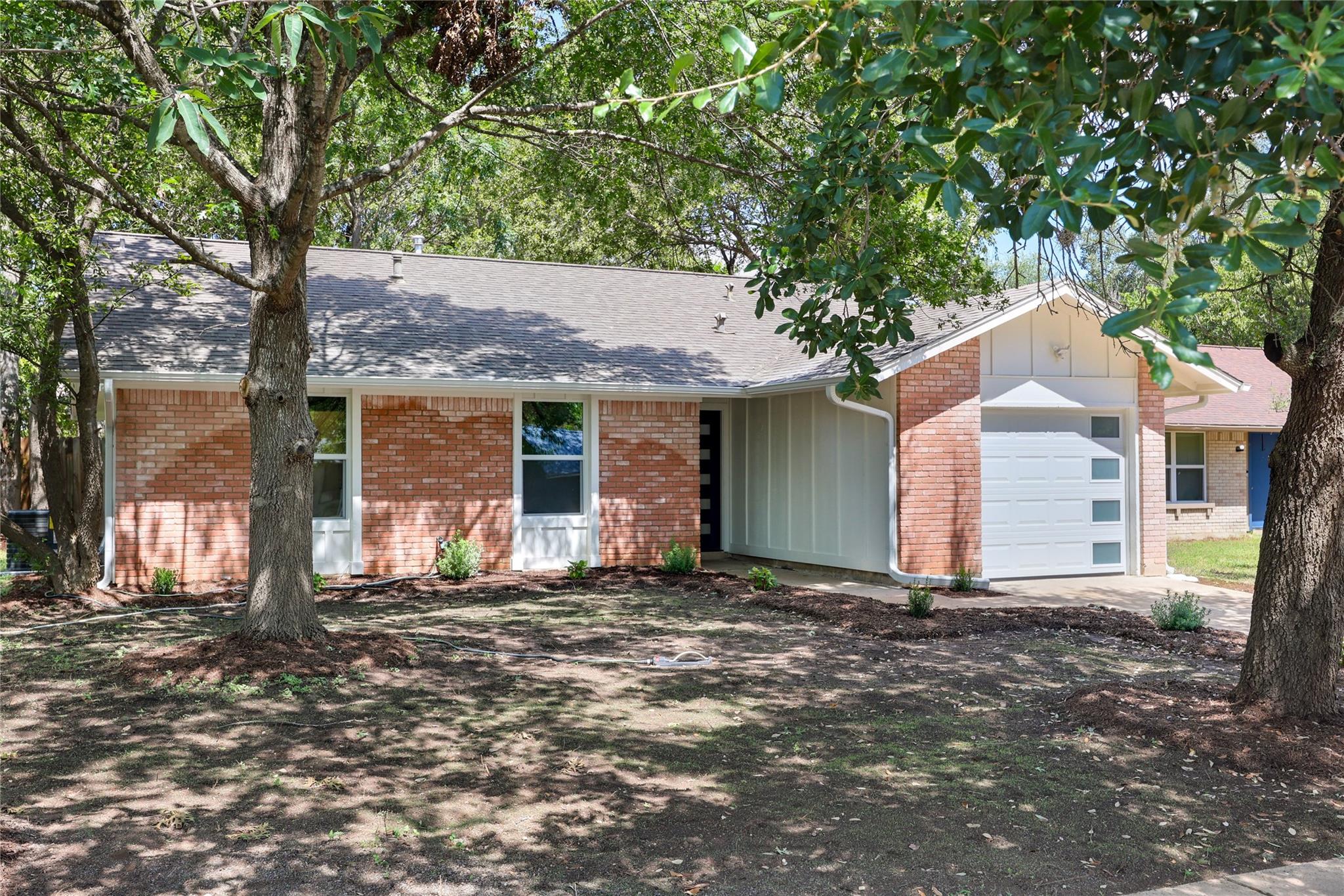Single-story brick house with an attached garage, recessed entry, and mature trees shading the front yard.