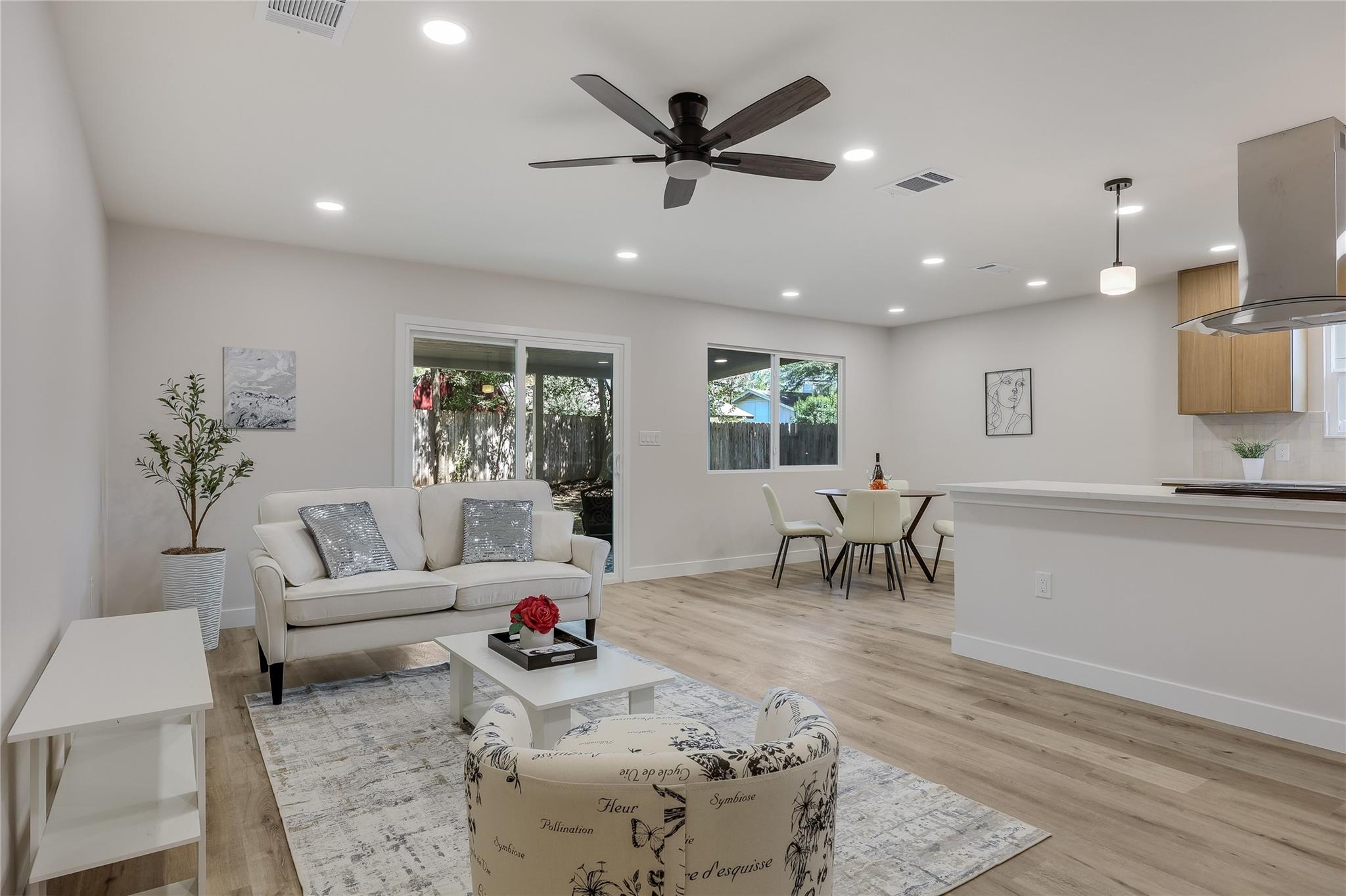Open-plan living room with a white sofa, patterned chair, dining area, and kitchen island.
