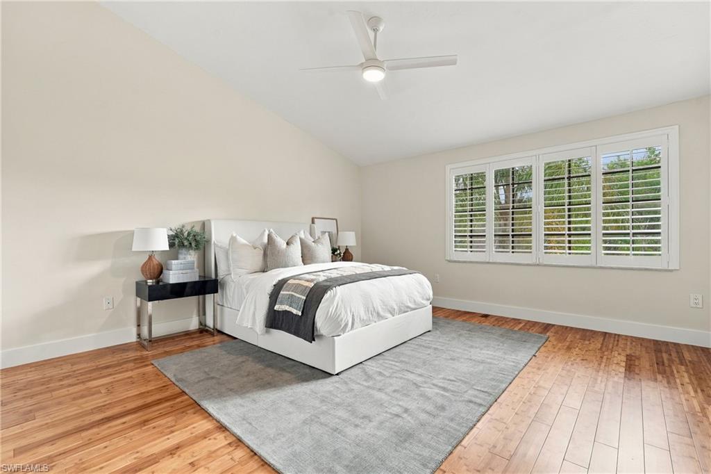 Staged bedroom with a white bed, gray rug, and wide shuttered windows.
