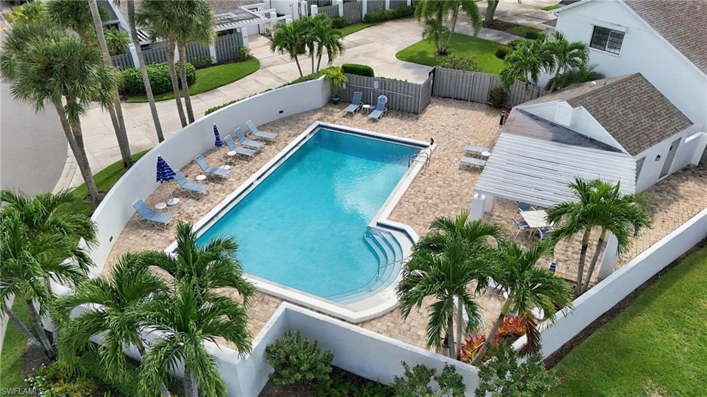 Aerial view of a turquoise pool courtyard with lounge chairs, palm trees, and a covered seating area.