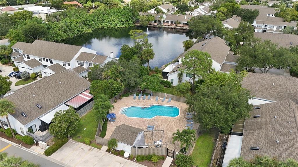 Aerial view of homes around a fenced swimming pool, with a pond and trees behind them.